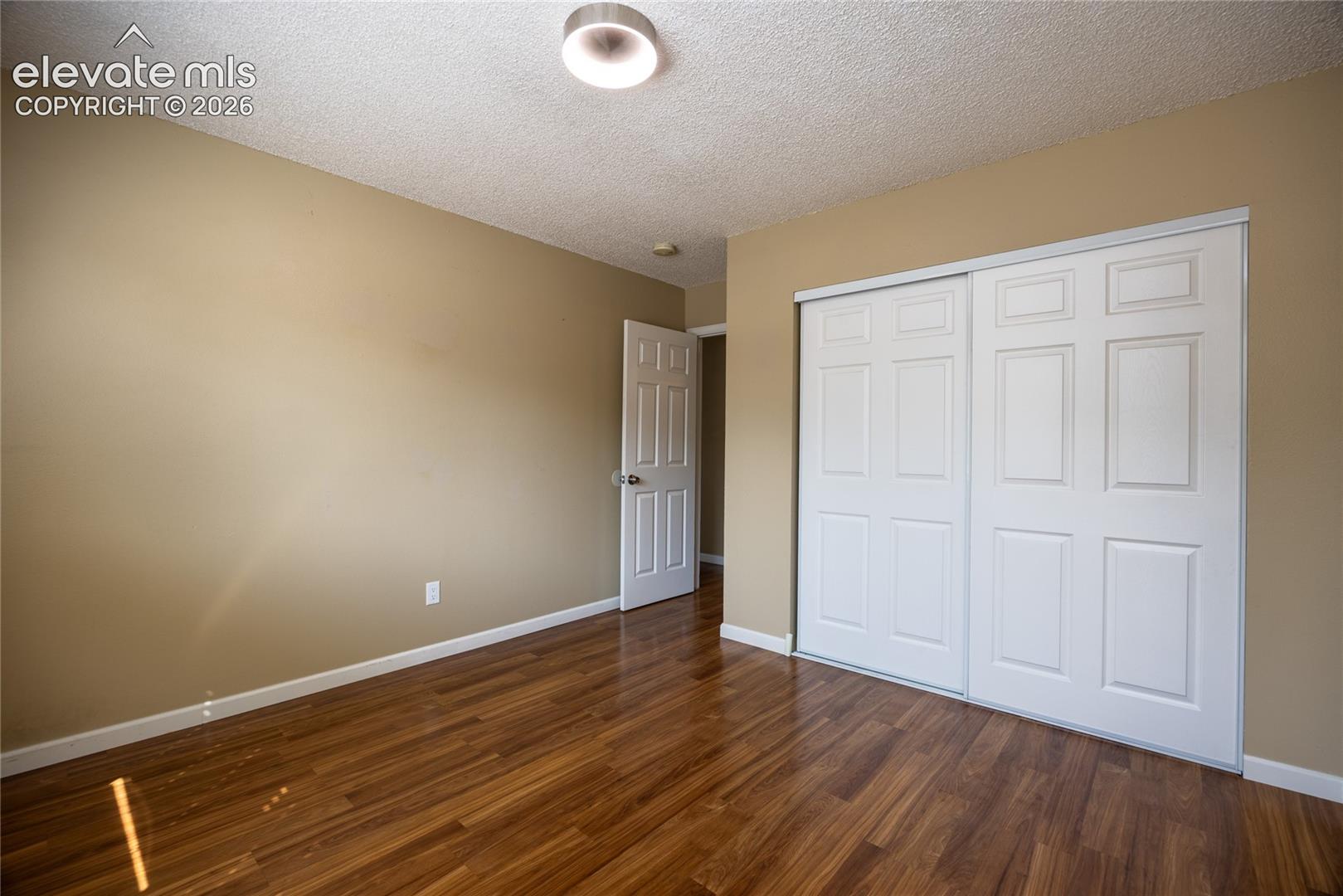 Wood-finish flooring with a ceiling-mounted light fixture, and white sliding closet doors