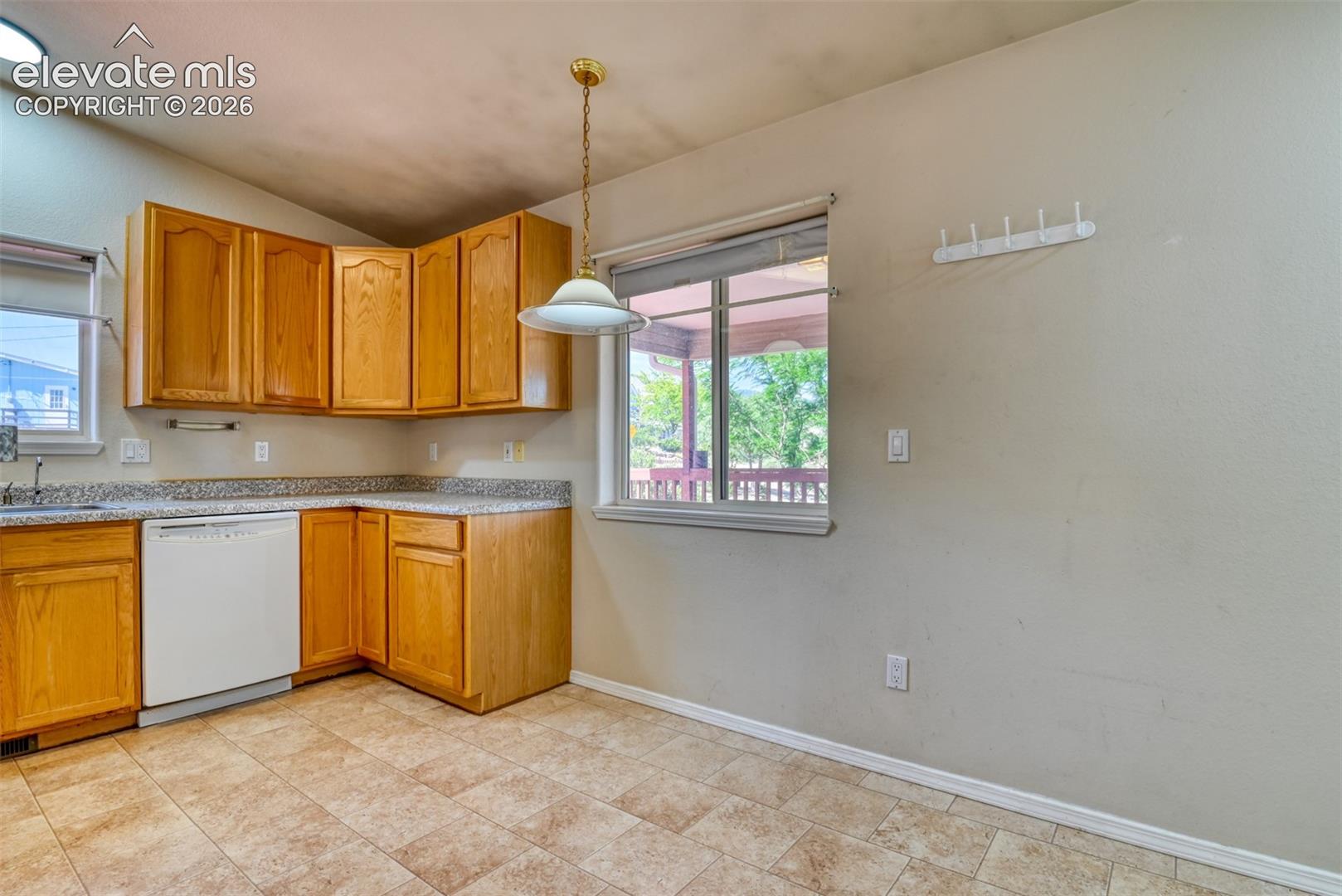 Kitchen area featuring wood cabinetry, stone-finish countertops, tile flooring, and a suspended pendant light fixture