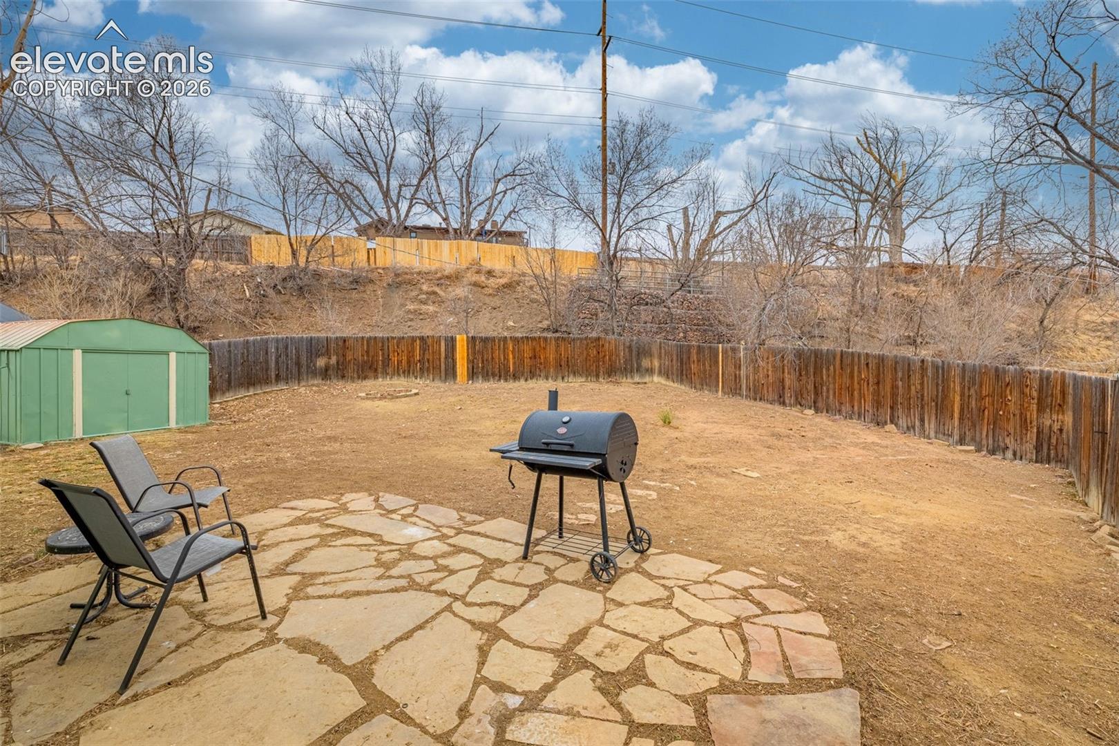 Backyard featuring a stone paver patio, full wood fencing, and a detached metal storage shed
