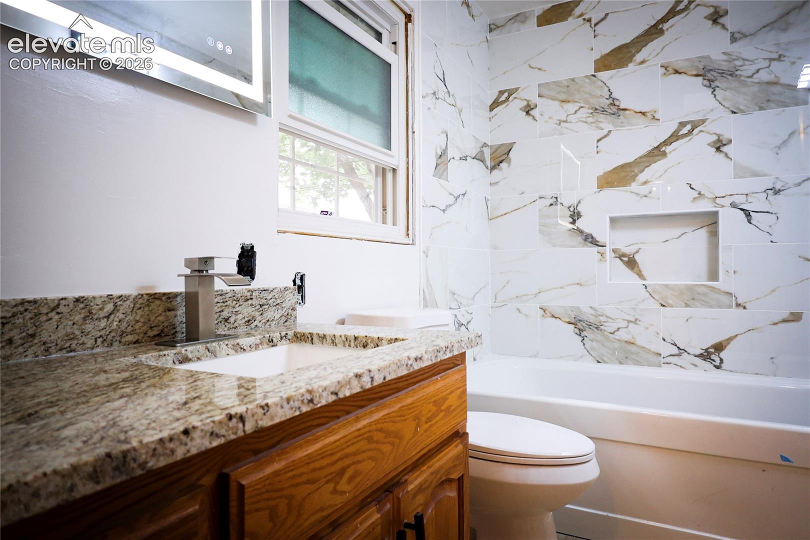 Main bath Vanity with granite countertop and integrated sink, modern faucet, and illuminated mirror