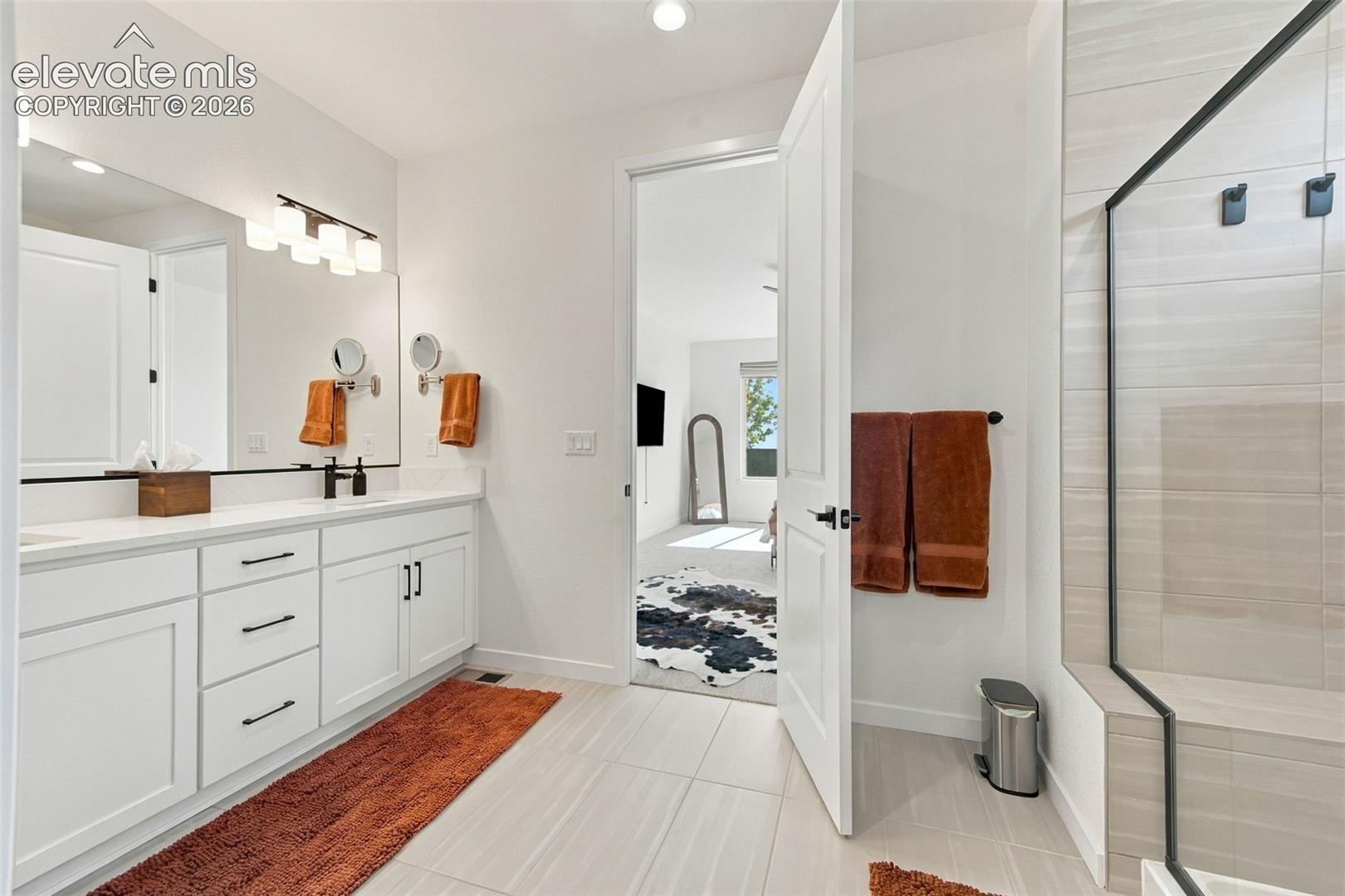 Bathroom featuring a white dual-sink vanity with matte black hardware, a large vanity mirror, recessed lighting, and a glass-enclosed shower with tiled walls