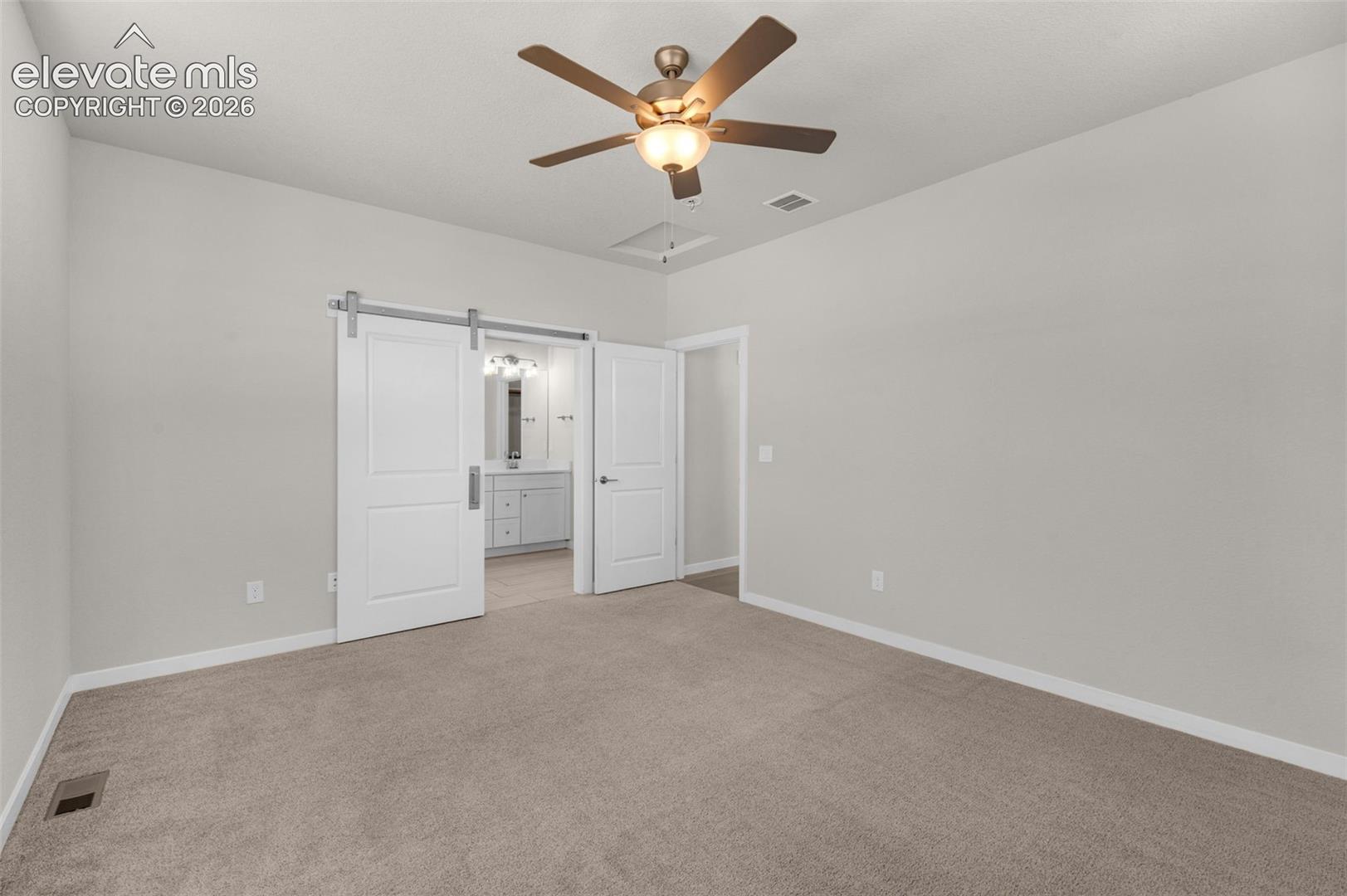Neutral-toned carpeted room featuring a ceiling fan with integrated lighting and sliding barn-style door hardware