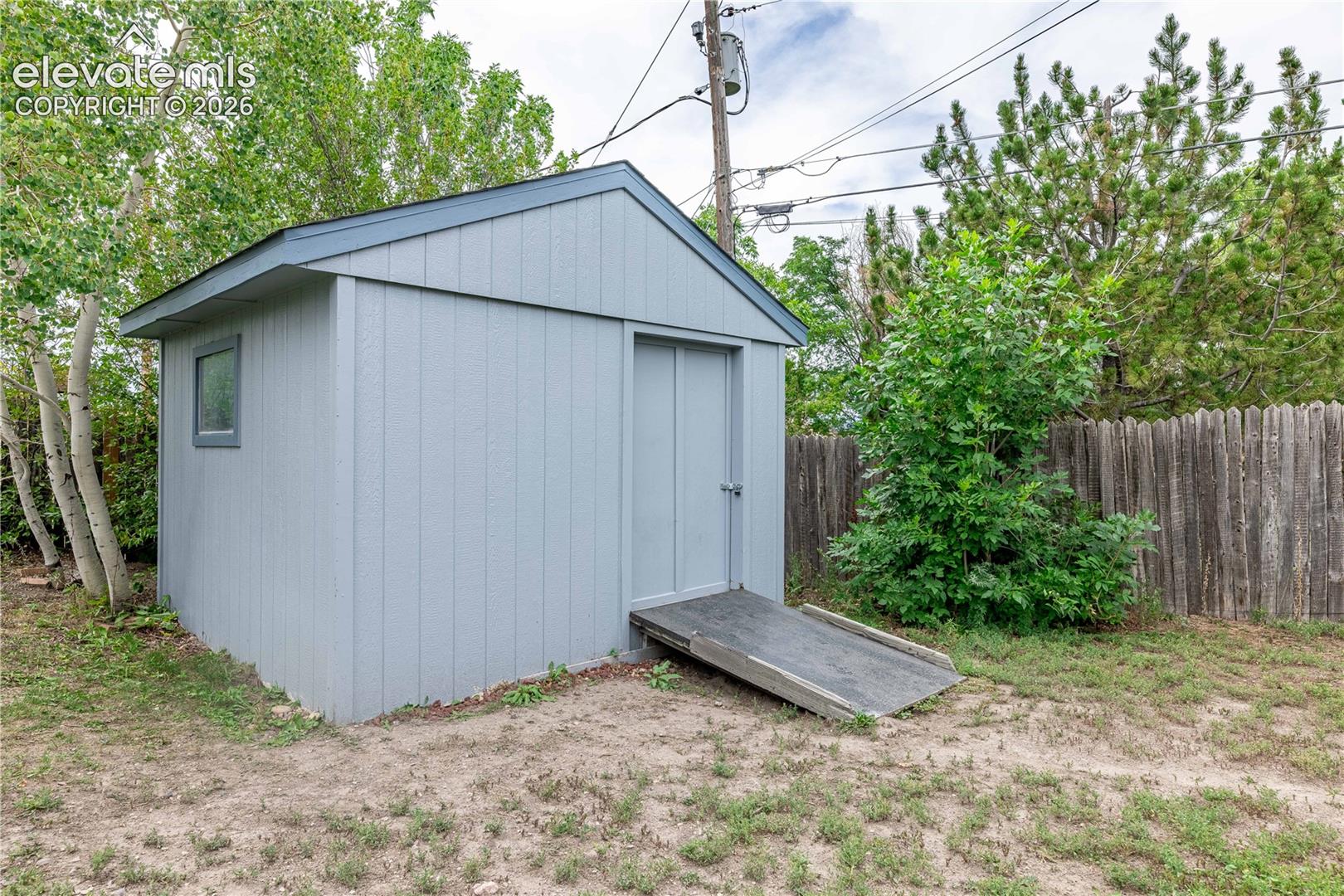 Exterior storage structure featuring vertical siding, a gabled roof, a single-entry door, and an attached ground-level ramp