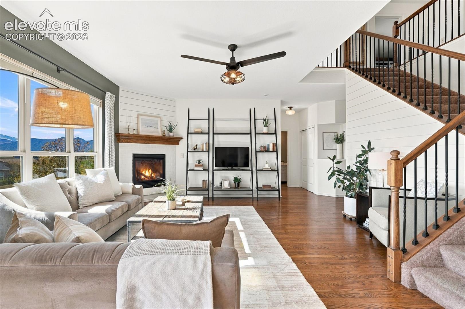 Open-concept living space featuring wood-finish flooring, a fireplace with a wood mantel, horizontal wall paneling, and an open staircase with a wood handrail and dark metal balusters