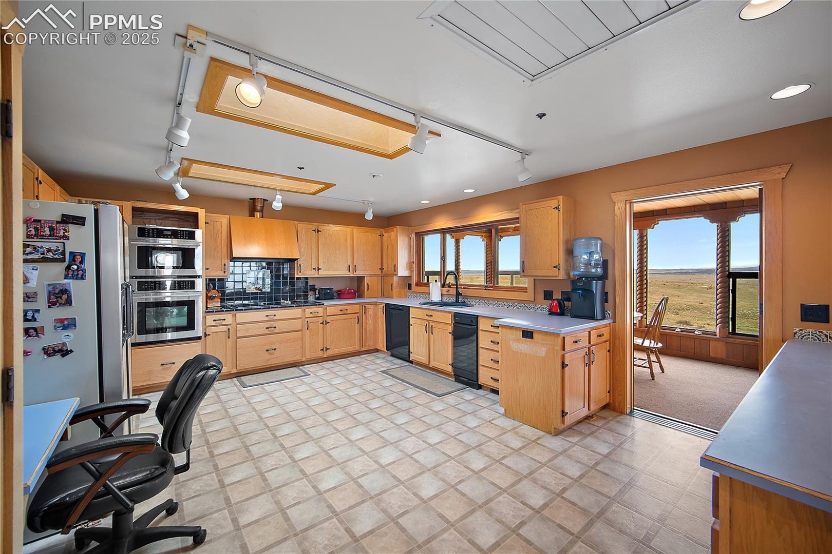 Kitchen featuring appliances with stainless steel finishes, rail lighting, light brown cabinets, custom range hood, and light floors
