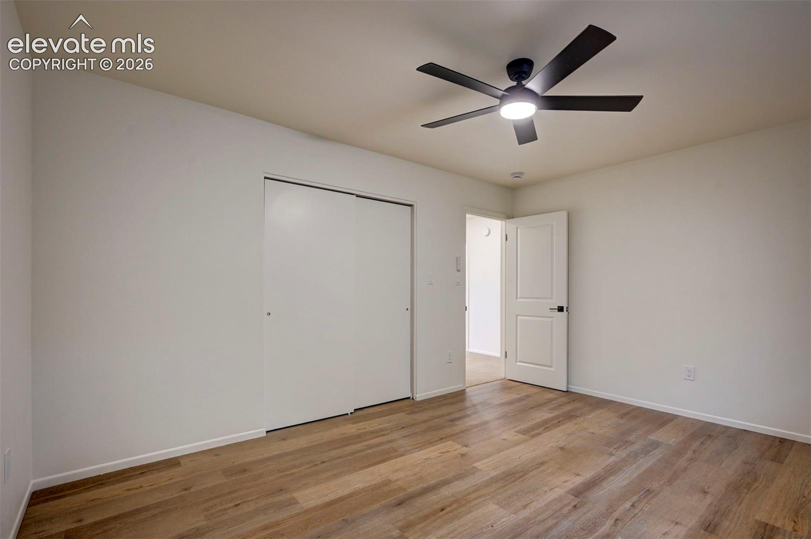 Room featuring wood-finish flooring, a ceiling fan with integrated lighting, and a sliding-door closet
