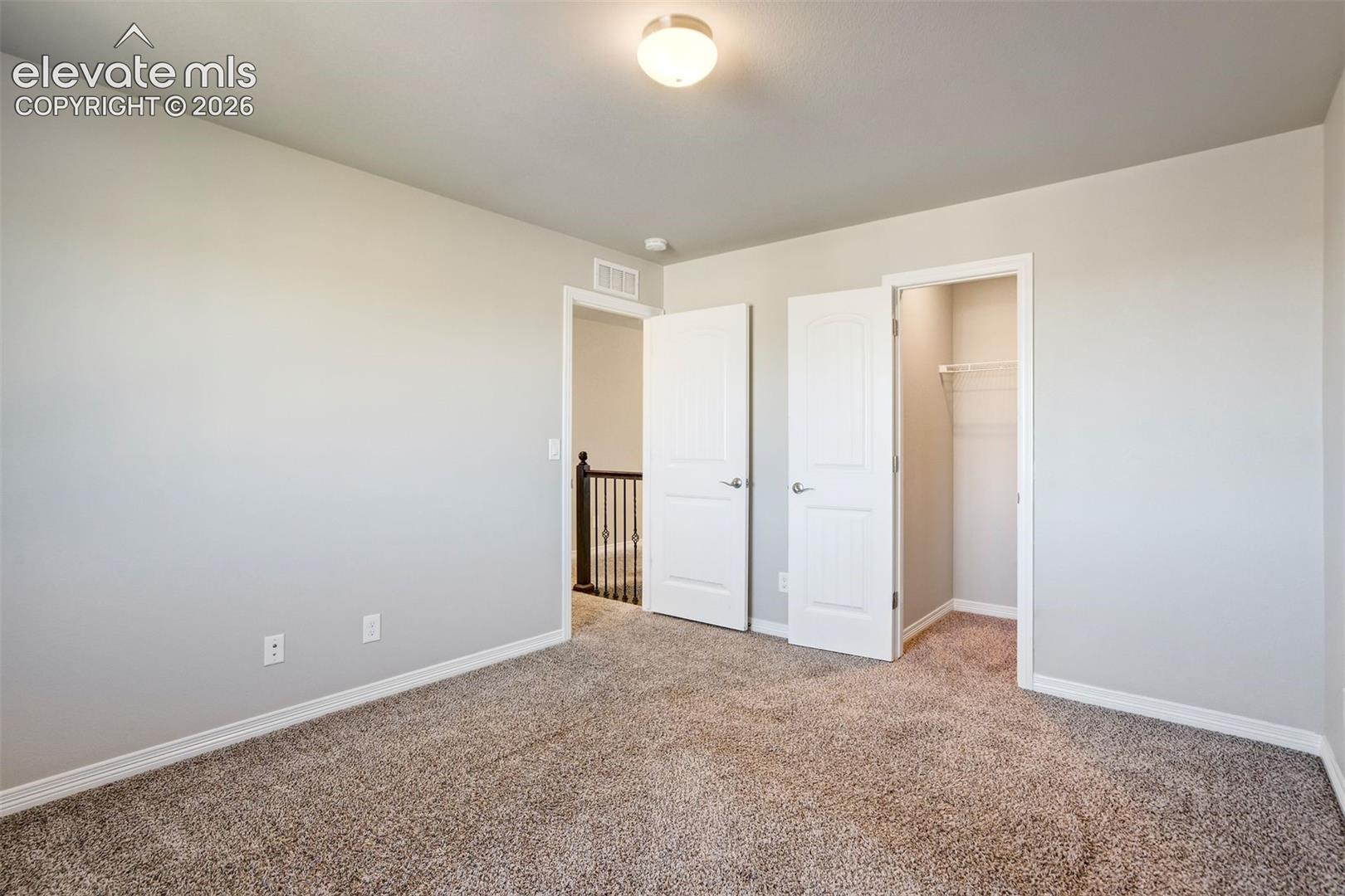 Neutral-toned walls, plush carpet flooring, recessed lighting, and a built-in closet with wire shelving