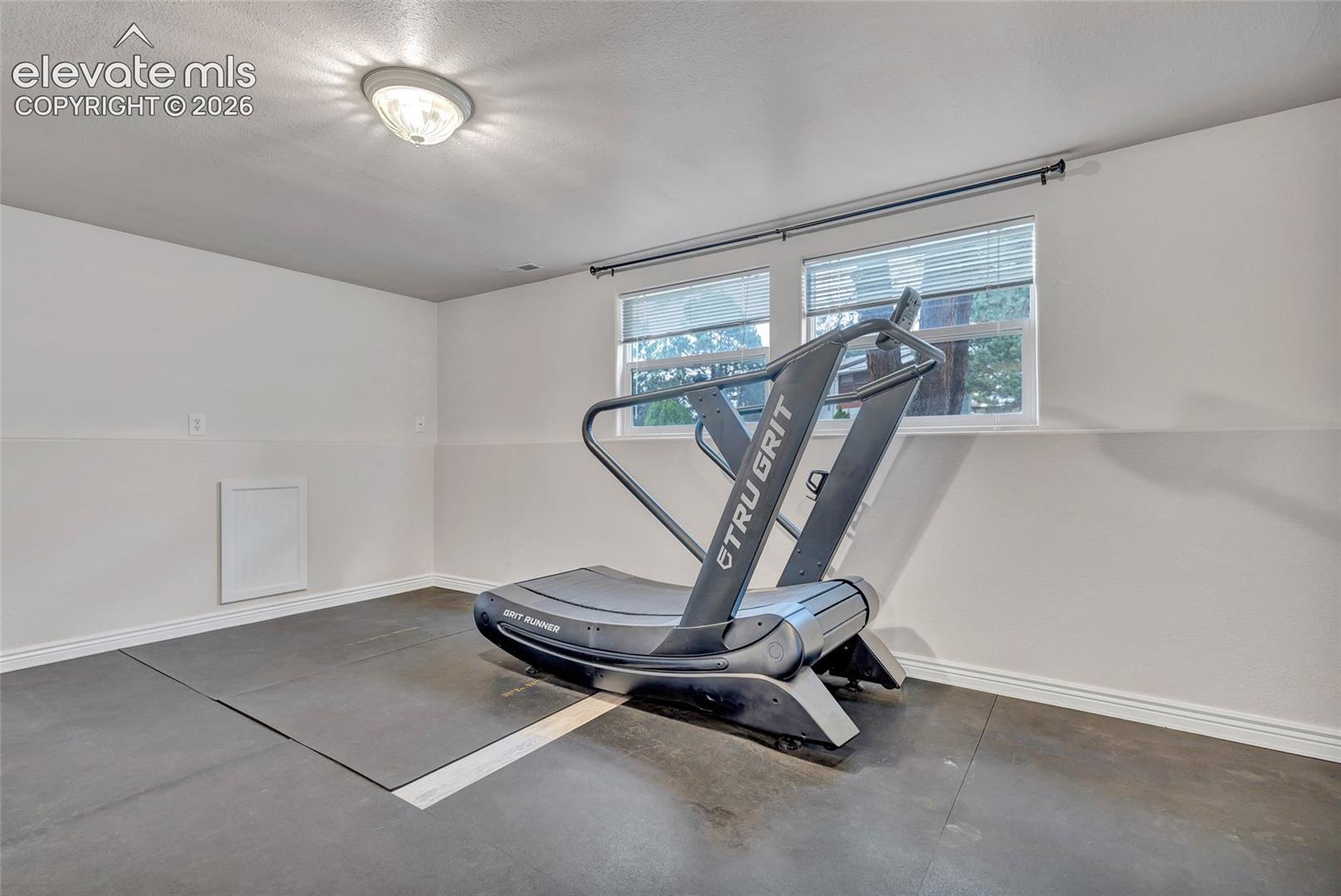 Recreational room featuring a flush-mount ceiling light, two windows with blinds, a white access panel, and dark rubber flooring