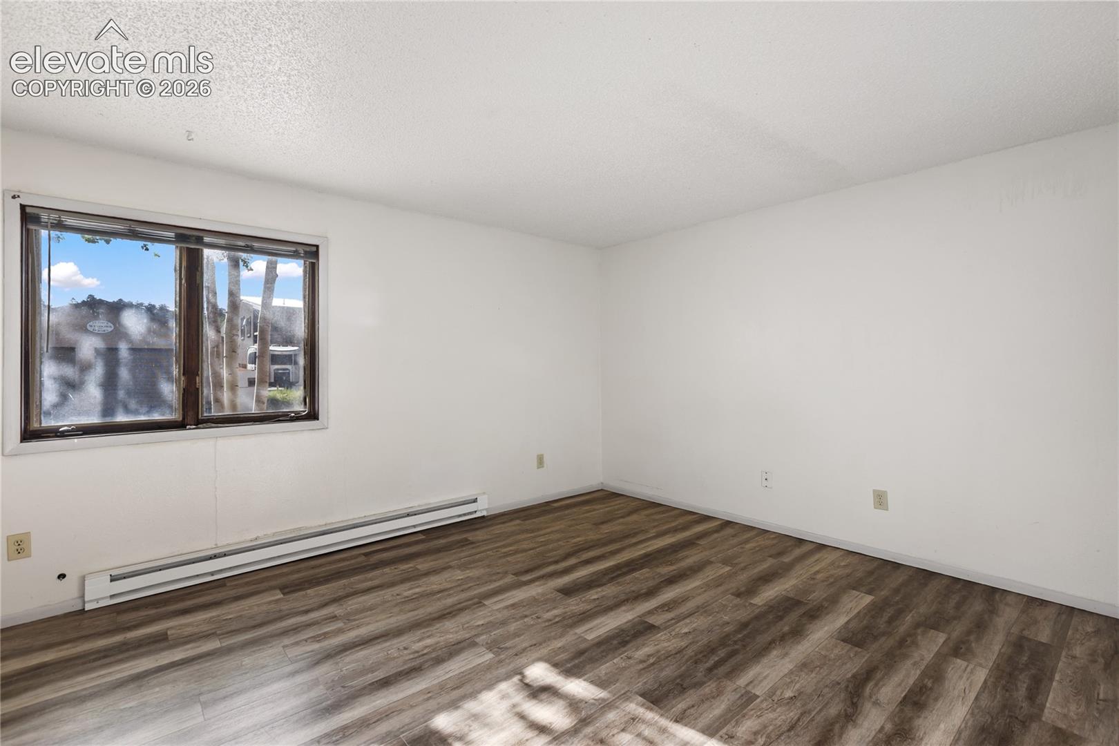 Spacious room featuring wood-finish flooring and white painted walls