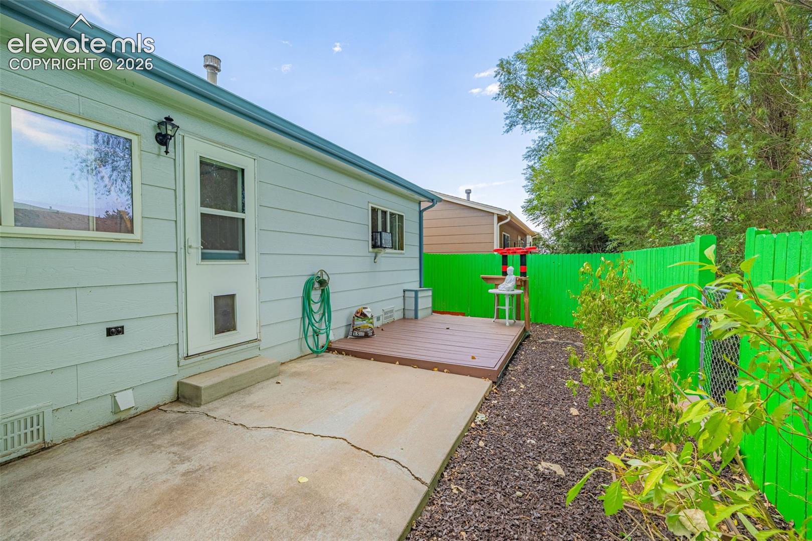 Rear exterior featuring light blue siding, a concrete patio, and a brown wood deck