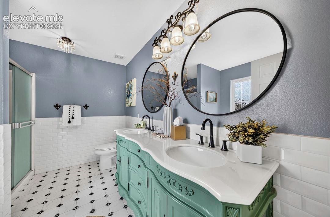 Double vanity featuring a light-toned countertop with integrated dual basins, matte black fixtures, oval mirrors, and ornate millwork cabinetry