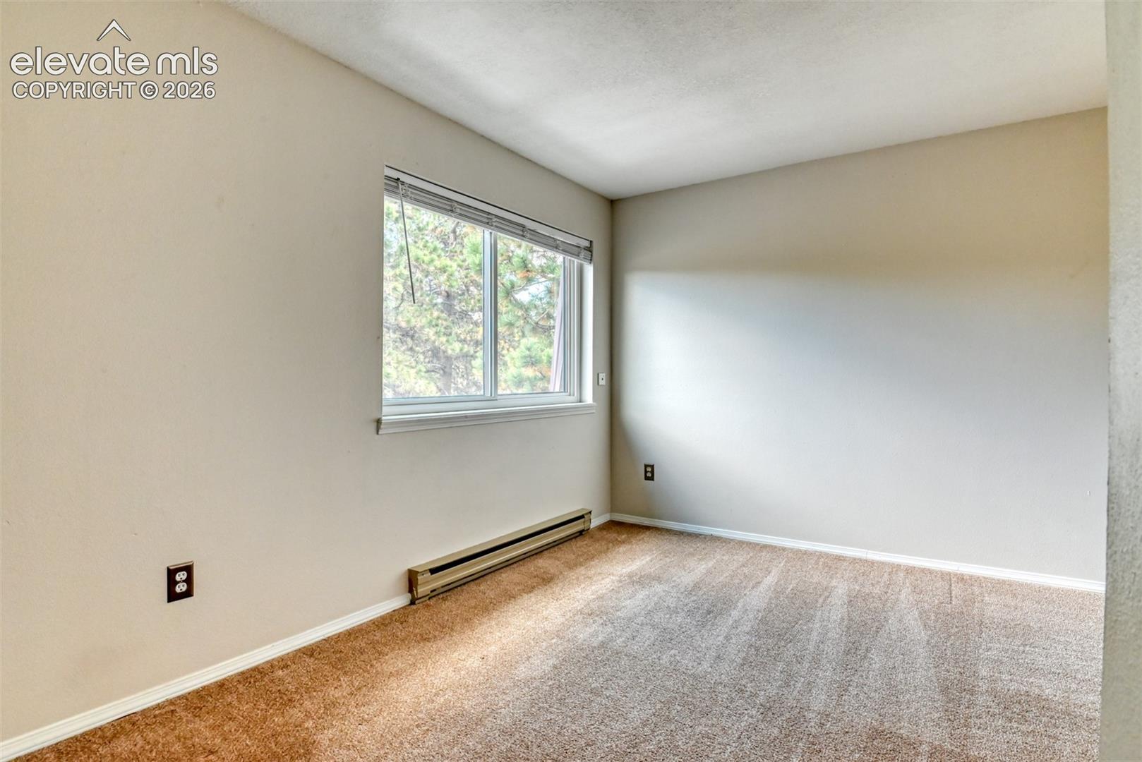 Neutral-toned carpeting, white window trim, and baseboard heating unit