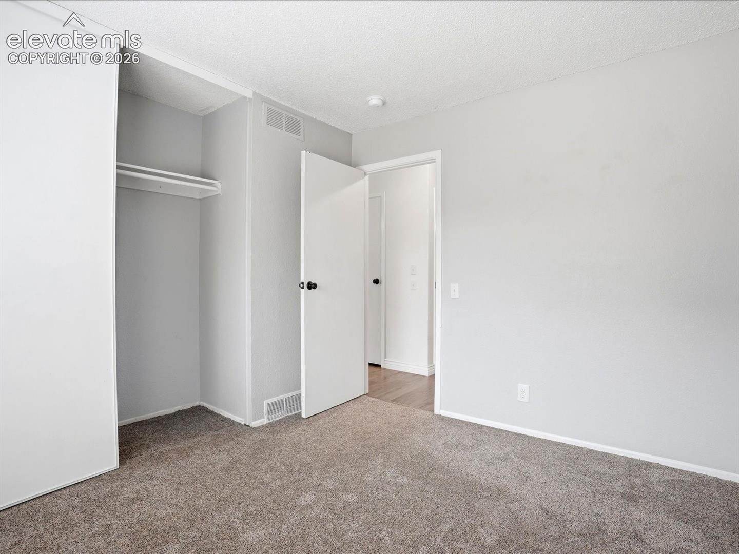 Neutral-toned interior space featuring wall-to-wall carpeting, a built-in closet with overhead shelving, and solid-core doors with matte black hardware