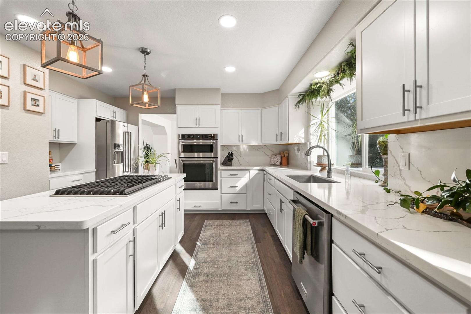 White shaker cabinetry with modern hardware, stainless steel appliances, wood-finish flooring, recessed lighting, and a kitchen island featuring a built-in cooktop