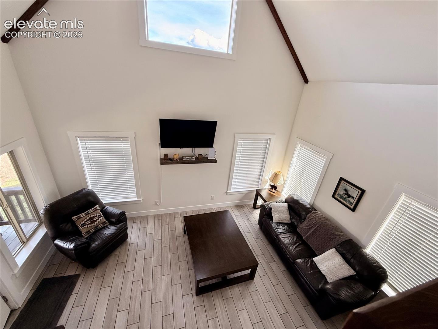 Vaulted ceilings with exposed beams, high transom window, light wood-finish flooring, and multiple windows with blinds