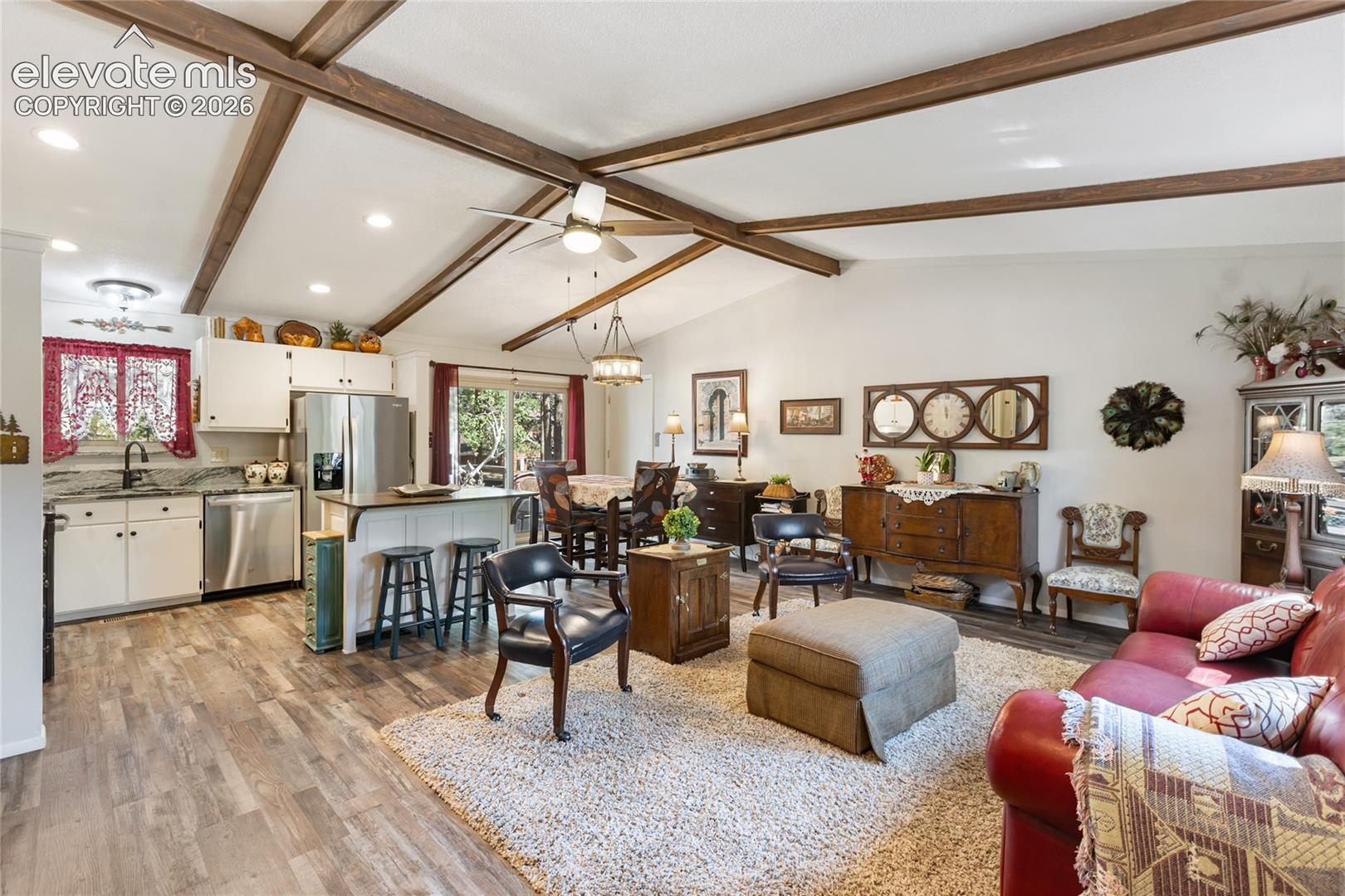 Vaulted ceiling with exposed wood beams, wood-finish flooring, white cabinetry, stainless steel appliances, and a kitchen island with seating