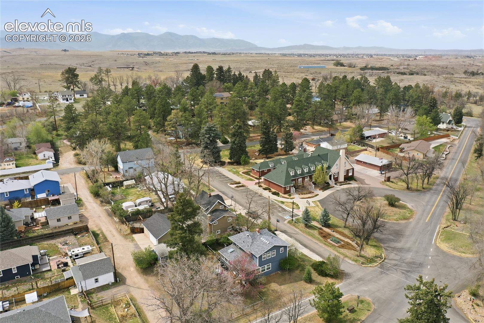 Aerial perspective featuring a residential setting with mature evergreen trees, paved roads, and a prominent mountain range backdrop
