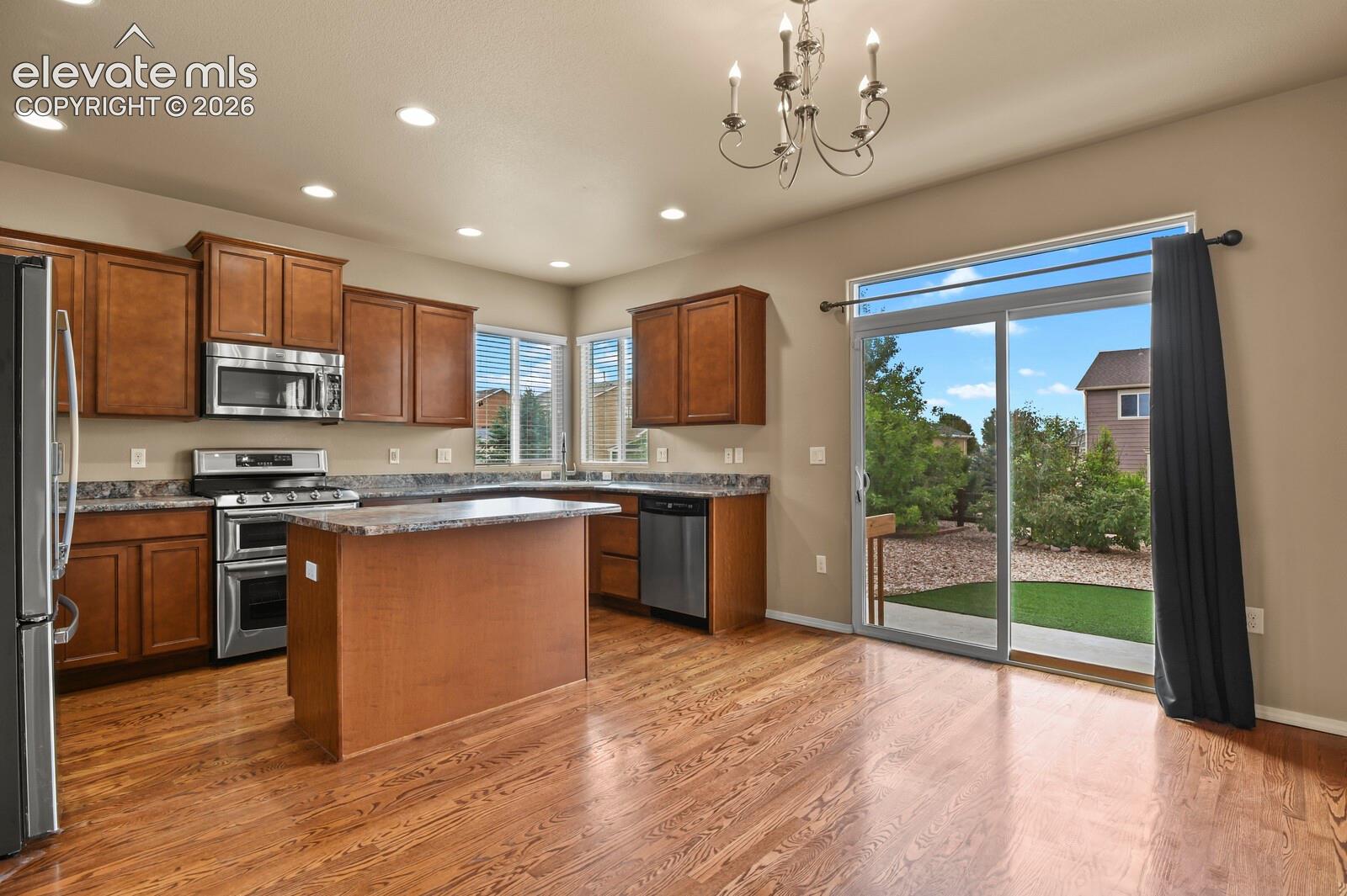 Wood-finish flooring throughout, complemented by a kitchen island with stone-finish countertop, stainless steel appliances, and wood cabinetry