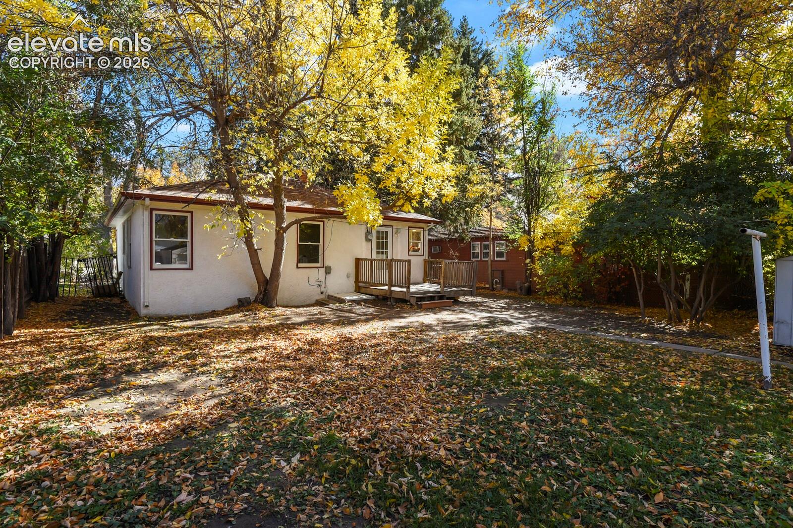 Exterior backyard featuring a raised wooden deck, stucco siding, and mature trees 