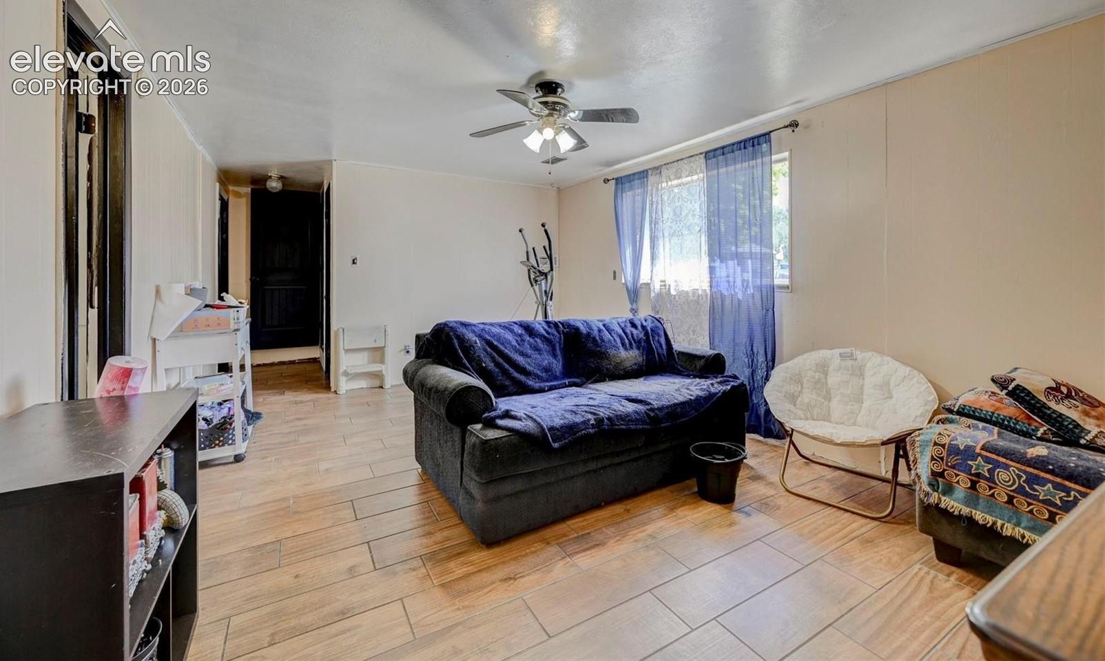 Living space featuring wood-finish tile flooring and a ceiling-mounted light fixture with a multi-blade fan