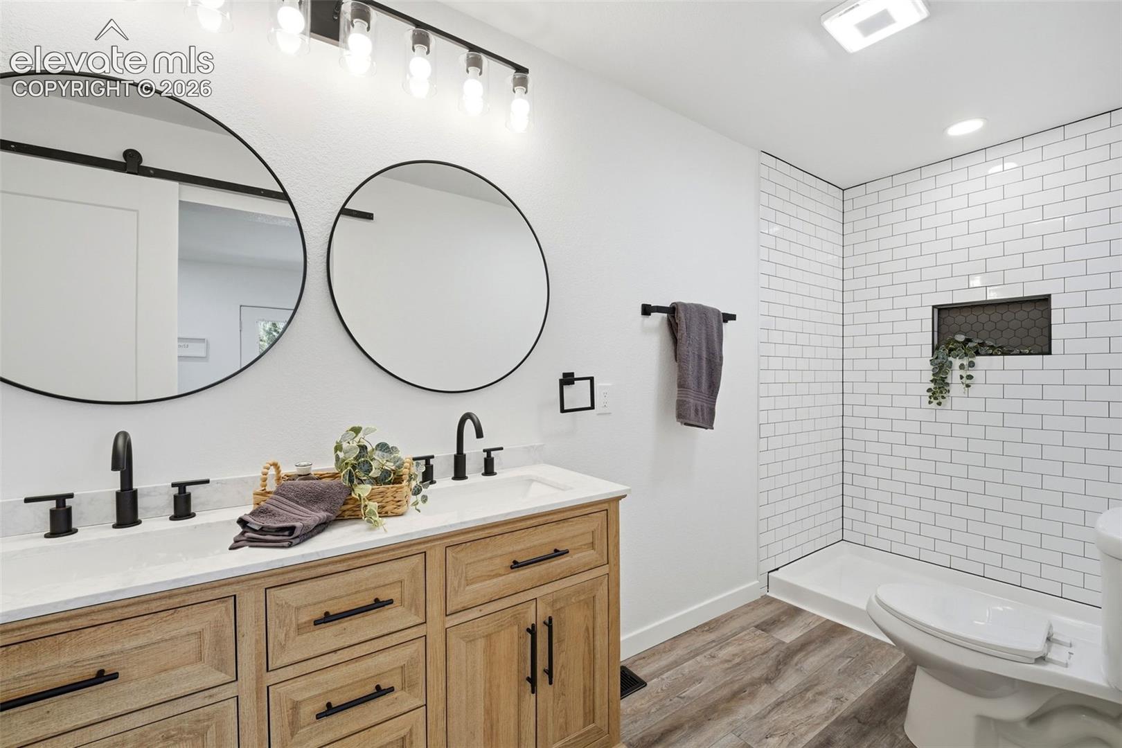 Dual round mirrors above a double vanity with stone-finish countertops and matte black fixtures