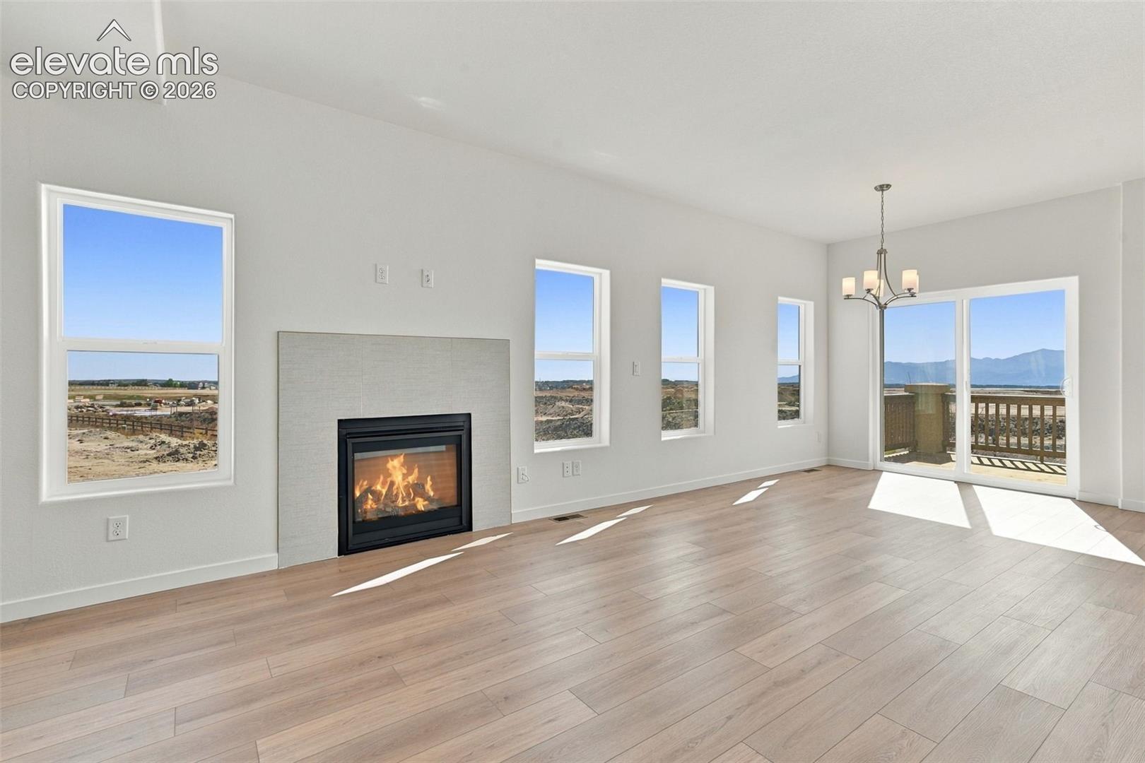 Spacious room featuring light wood-finish flooring, a tiled fireplace with a black surround, multiple windows, and a sliding glass door