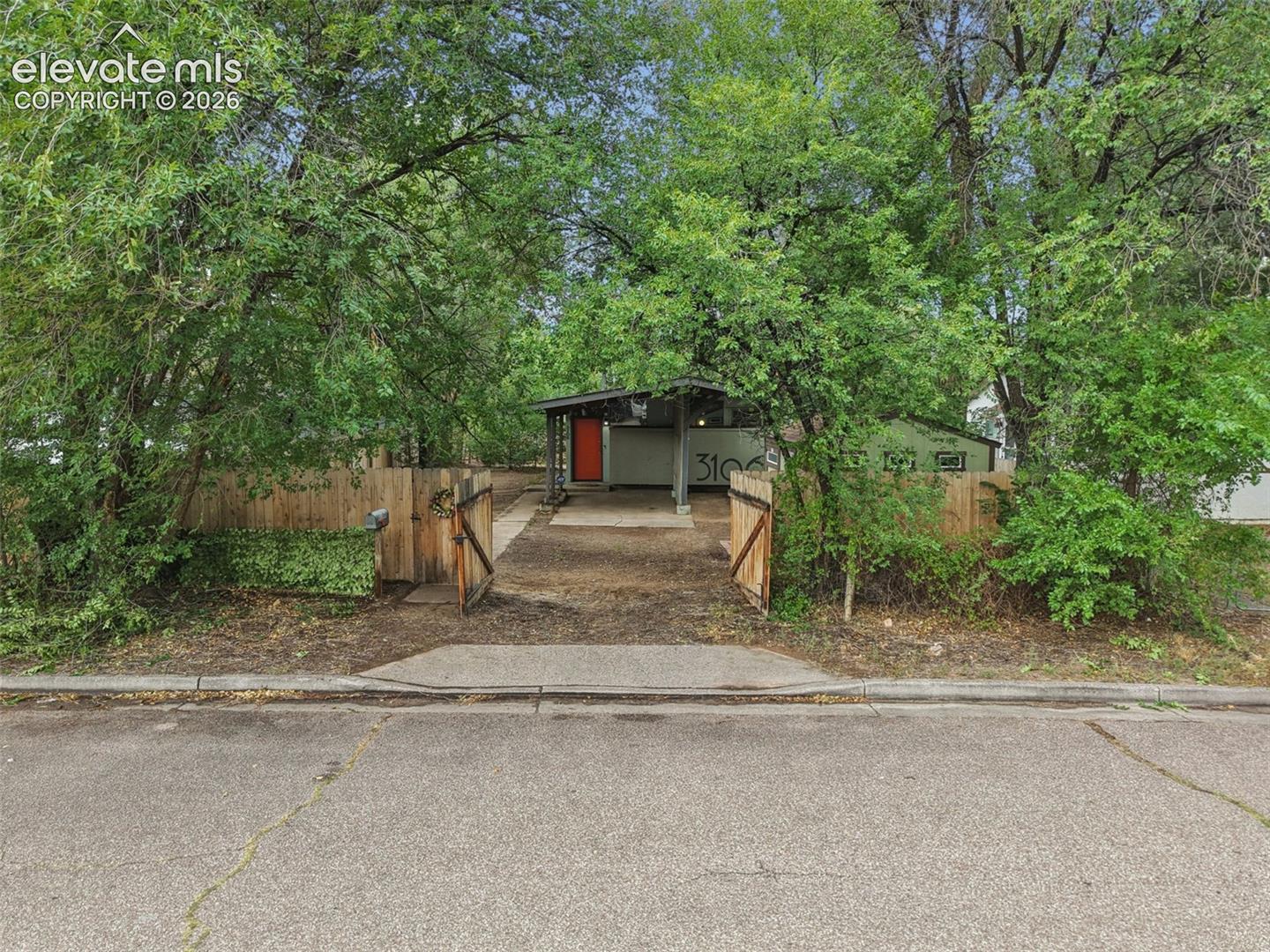 Gated entry with a wooden fence, asphalt driveway, and mature landscaping