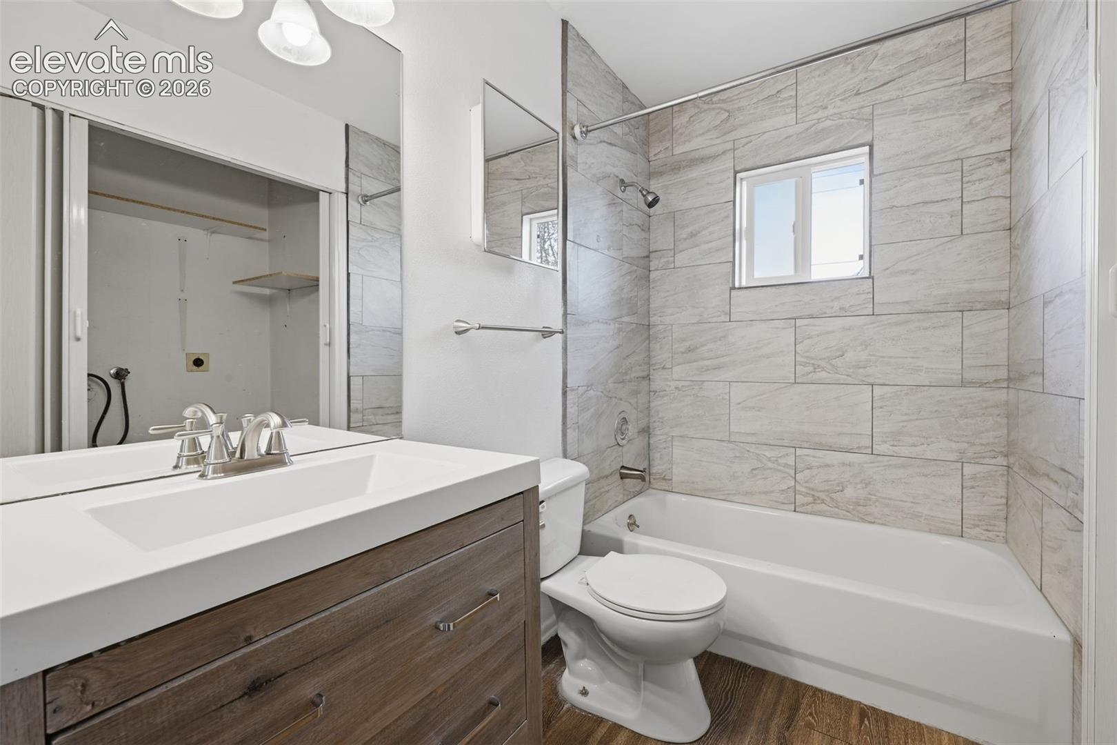 Wood-finish flooring with a white vanity featuring an integrated sink, brushed nickel faucet, and a large mirror