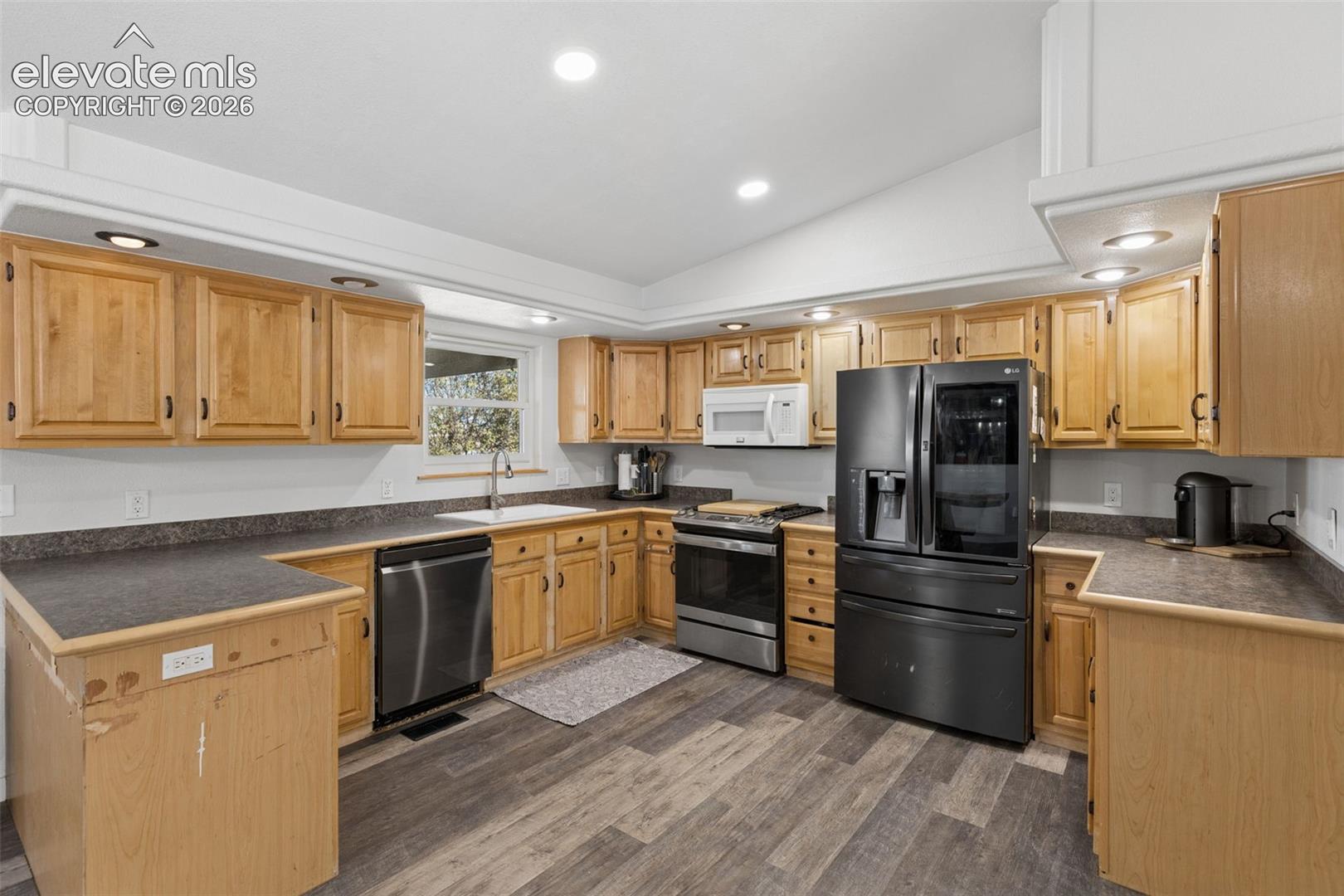 Kitchen featuring wood cabinetry, dark-finish countertops, stainless steel appliance suite, recessed lighting, and wood-finish flooring
