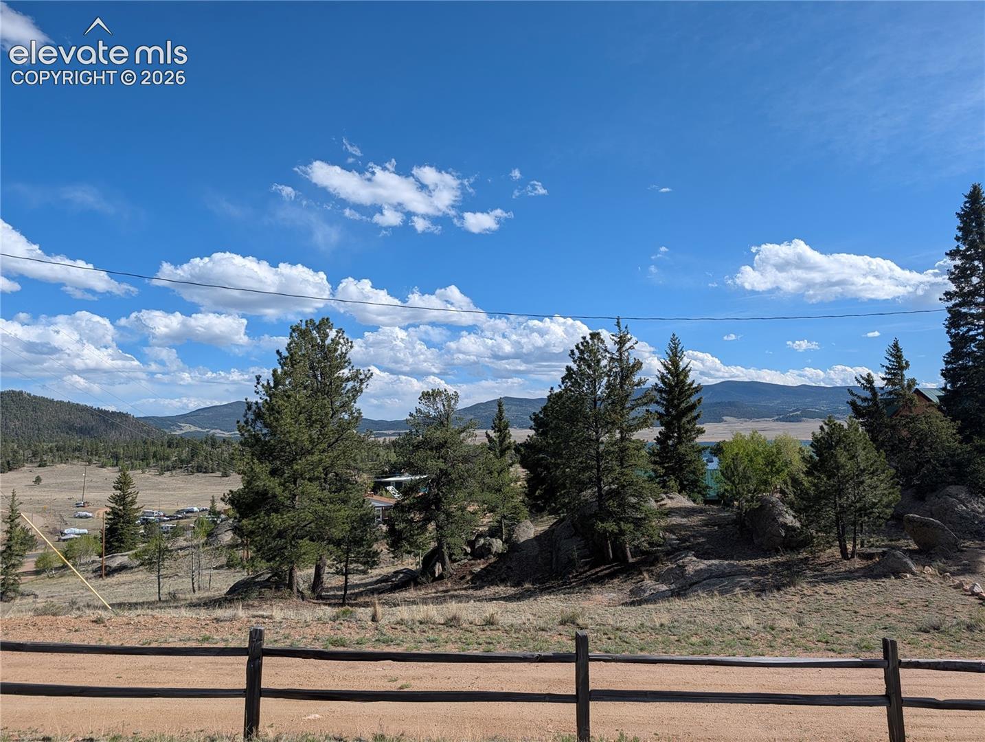 Expansive mountainous terrain with varied tree coverage, natural rock formations, and a split-rail fence