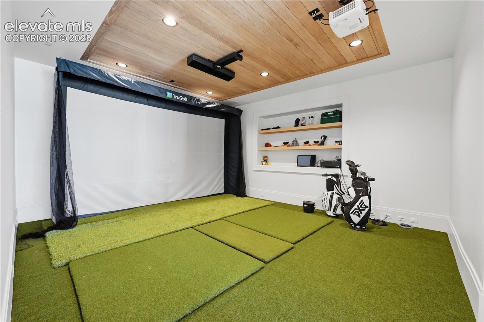Dedicated simulation room featuring a wood-plank recessed ceiling, inset shelving, recessed lighting, and integrated golf simulation equipment