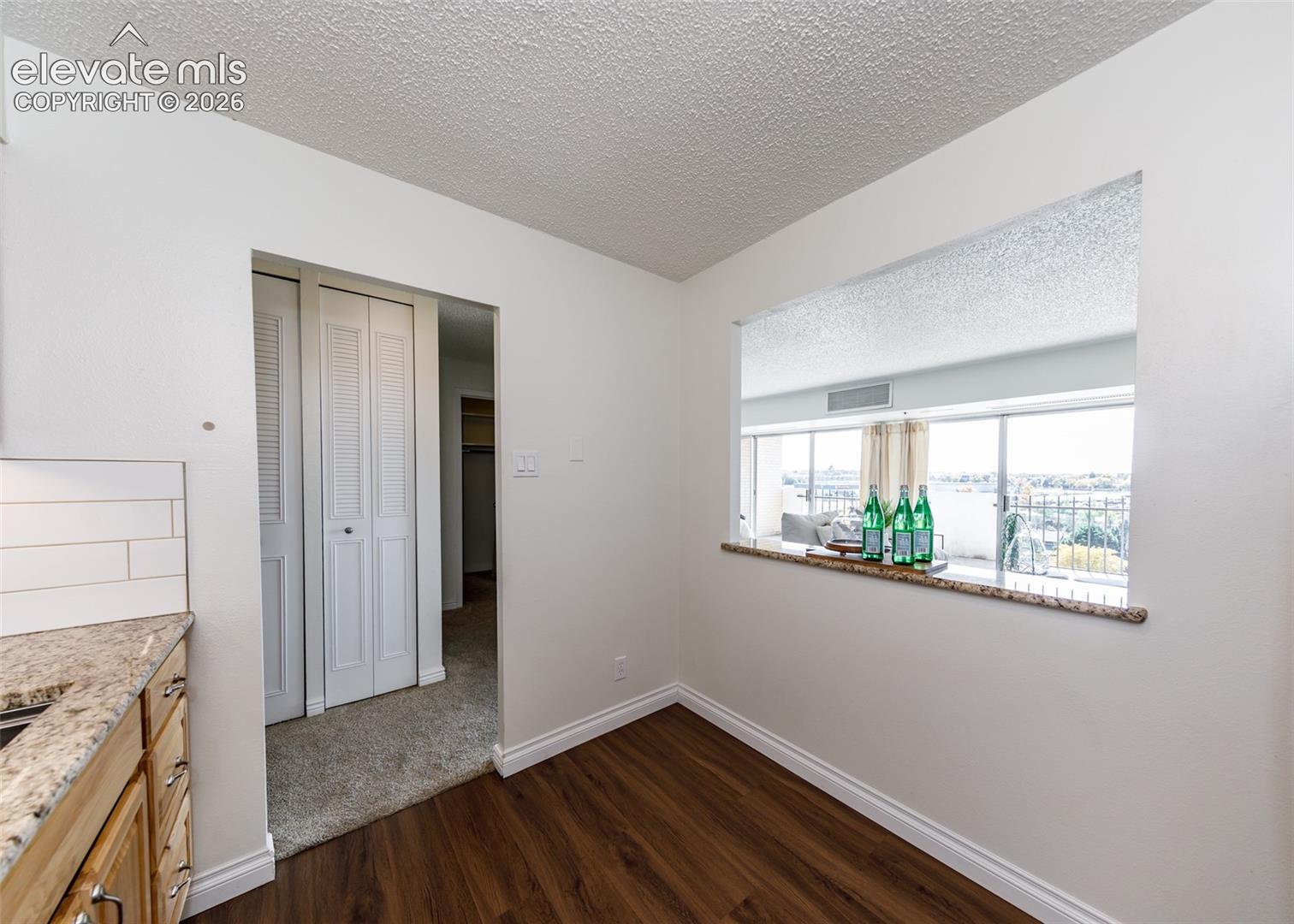 Pass-through opening with stone-finish countertop, wood-finish flooring, white louvered-door closet, and white subway tile backsplash