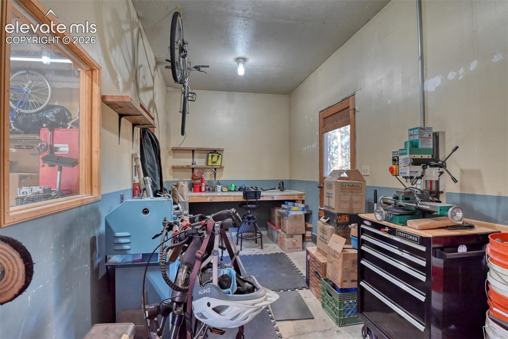 Workshop area featuring built-in wooden shelving, a fixed wooden workbench, an interior glass window, and a dedicated exterior access door