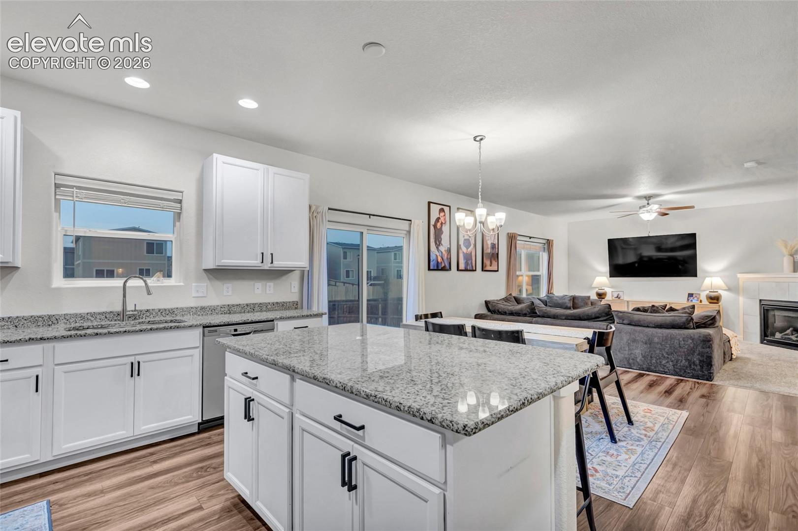 Kitchen island with granite countertop, white cabinetry, wood-finish flooring, recessed lighting, and sliding glass door