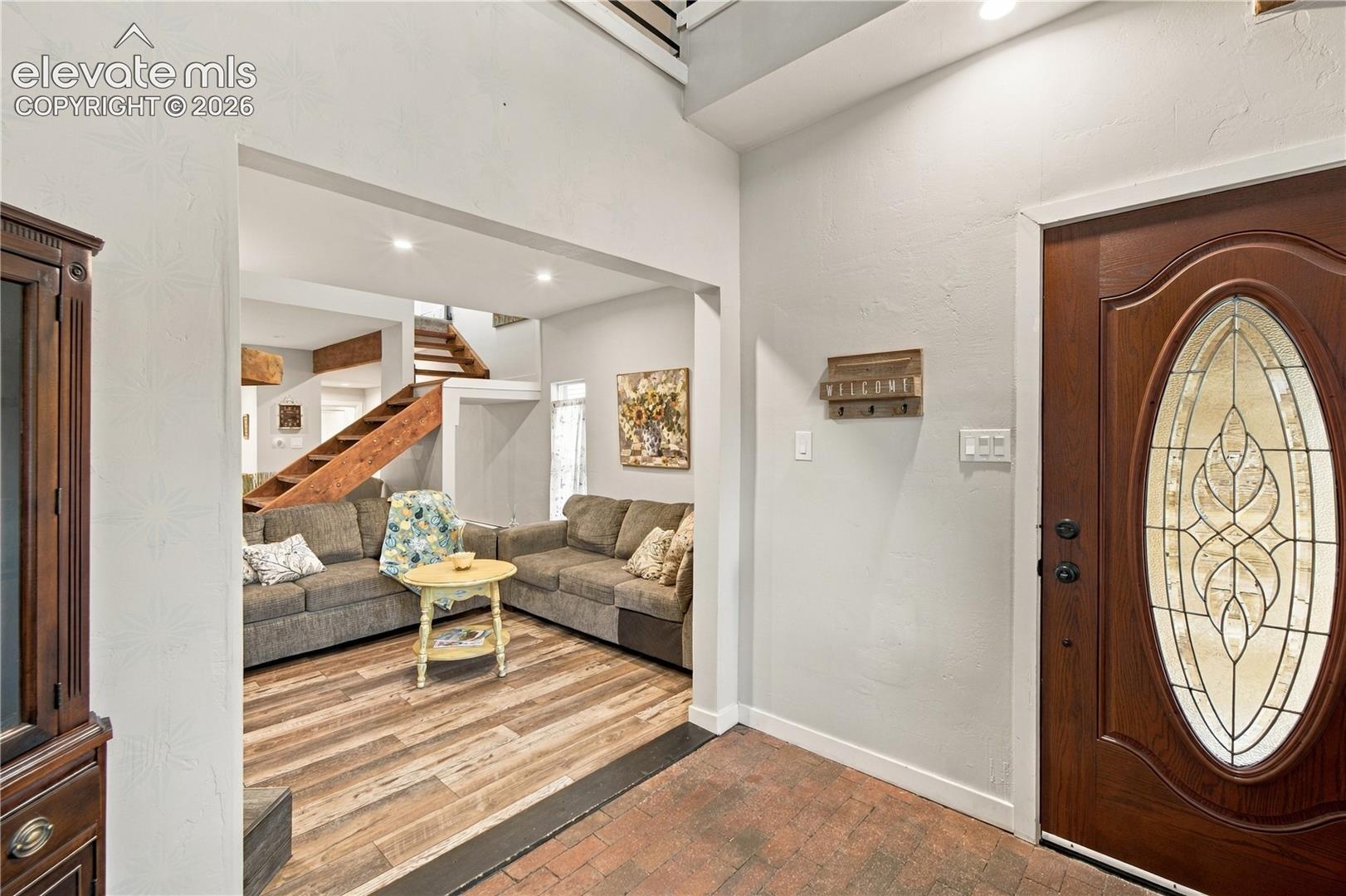 Entryway featuring a solid wood front door with oval glass insert, brick flooring, and wood-finish flooring with a wooden staircase
