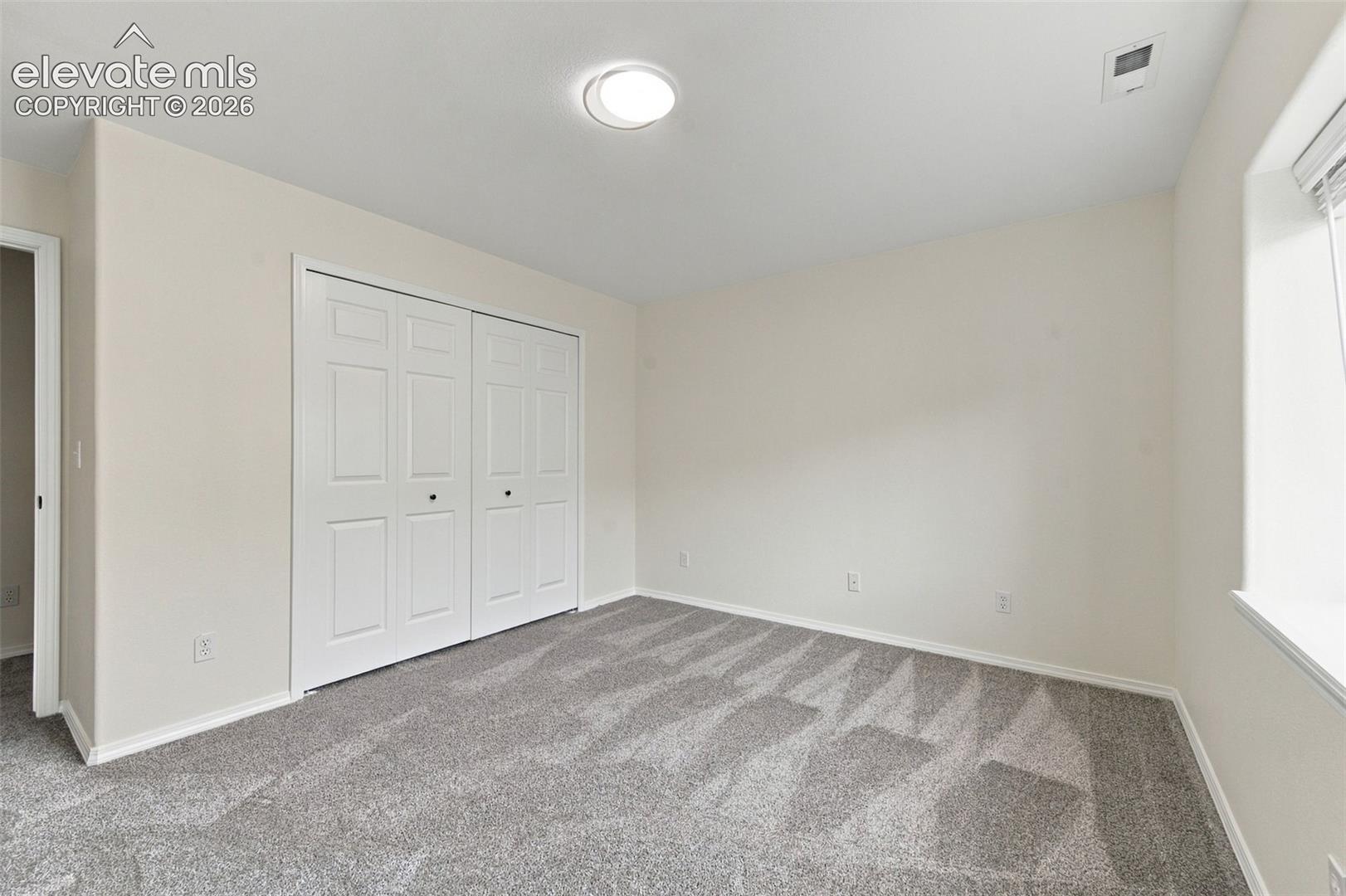 Neutral-toned interior room featuring wall-to-wall carpeting, white dual-panel closet doors, and recessed ceiling lighting