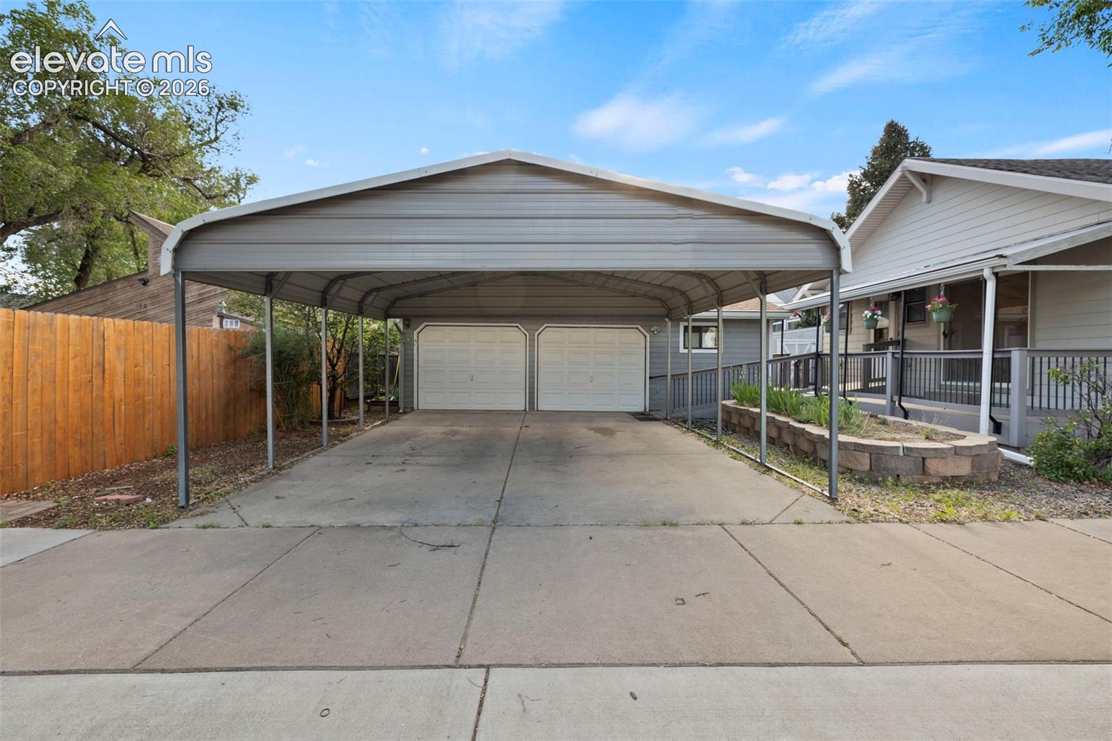 Covered carport with concrete driveway leading to two garage doors