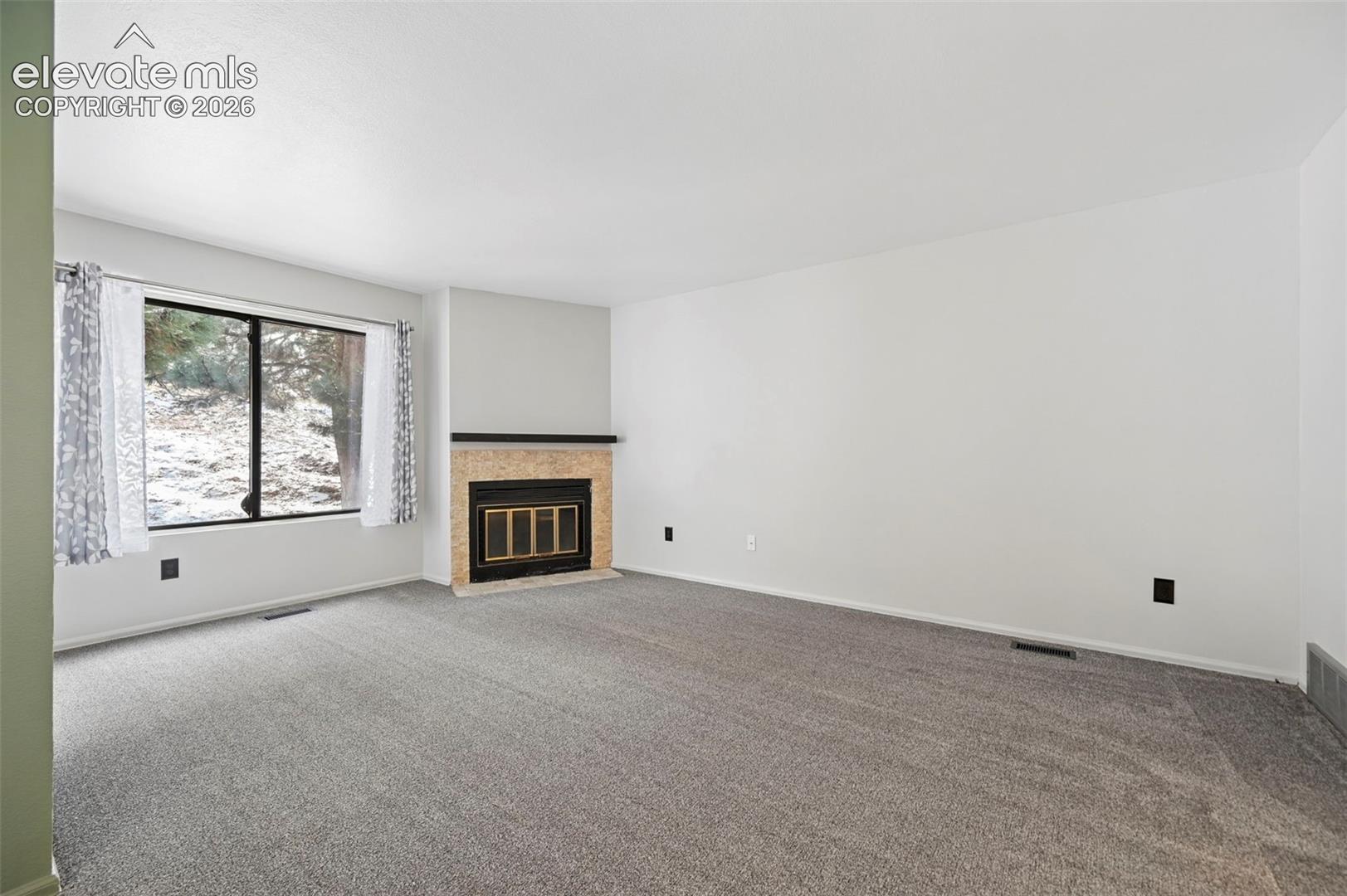 Recessed fireplace with a stone surround, large window, and gray carpeting