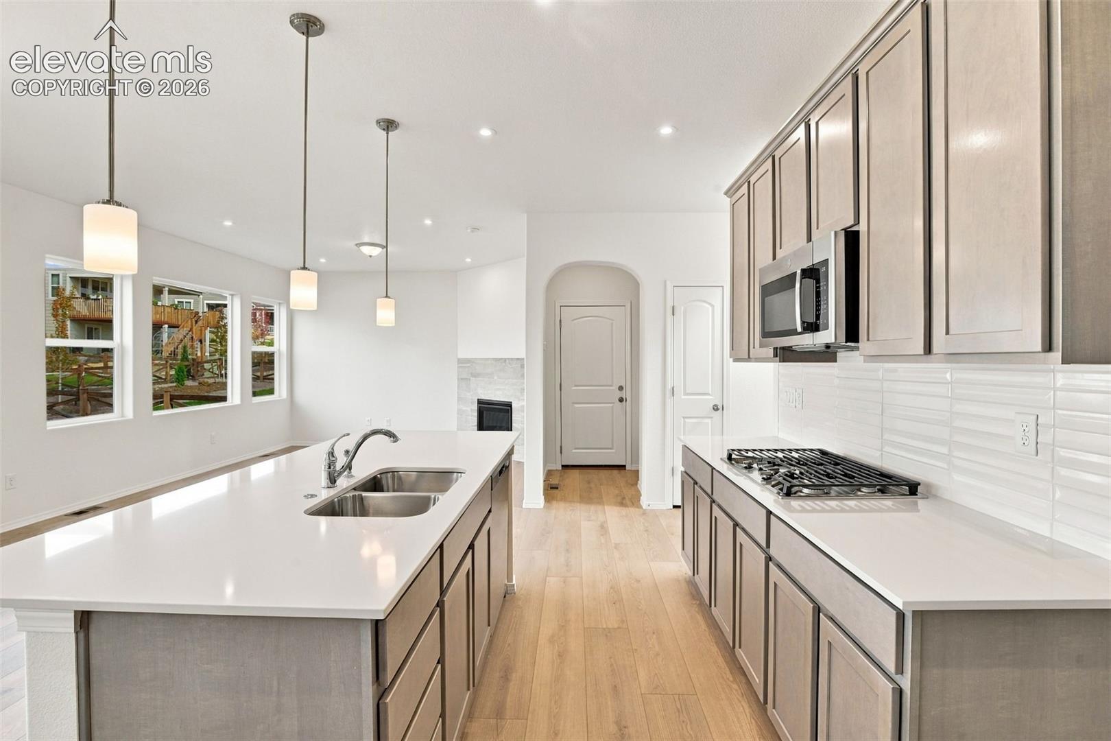 Kitchen featuring light-toned cabinetry, quartz countertops, a double-basin stainless steel sink, wood-finish flooring, and pendant lighting