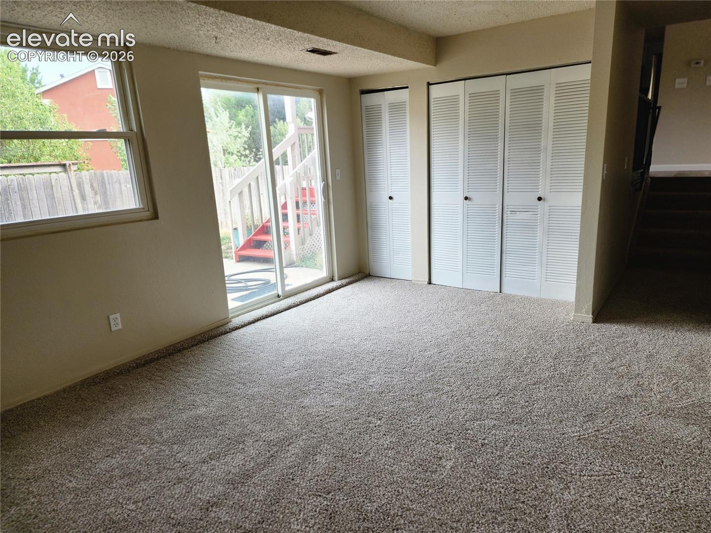 Carpeted room featuring a double-pane window, sliding glass door, and two sets of louvered bifold closet doors