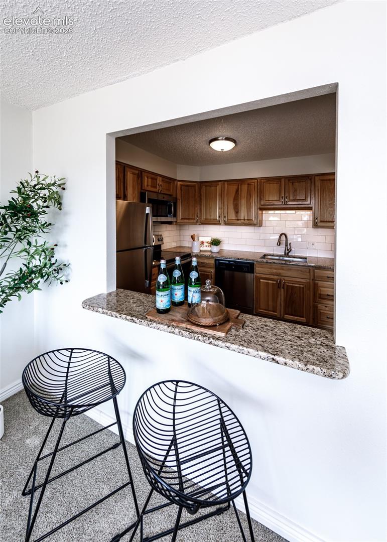 Kitchen pass-through featuring a granite countertop, wood-finish cabinetry, stainless steel appliances, and a subway tile backsplash