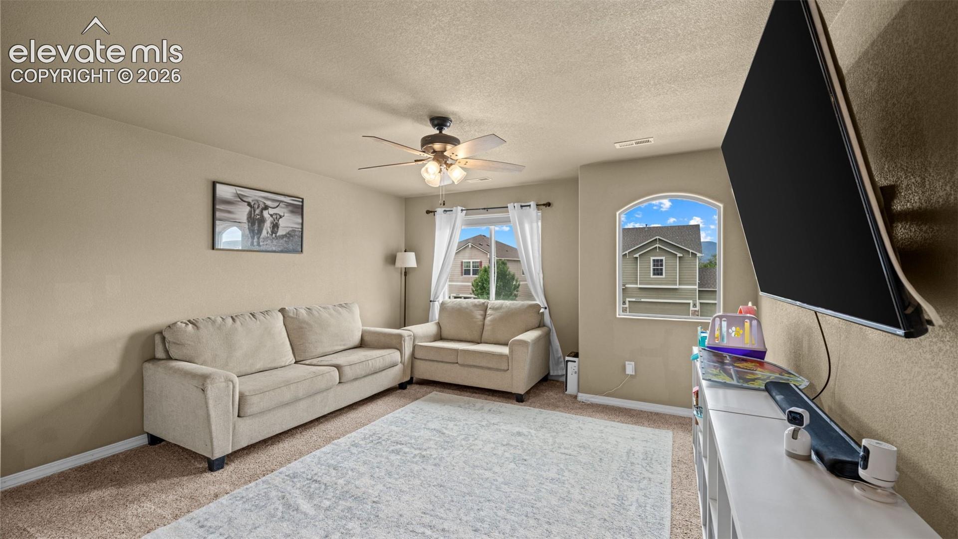 Carpeted room featuring a ceiling fan with integrated lighting, a large arched window, and neutral wall tones