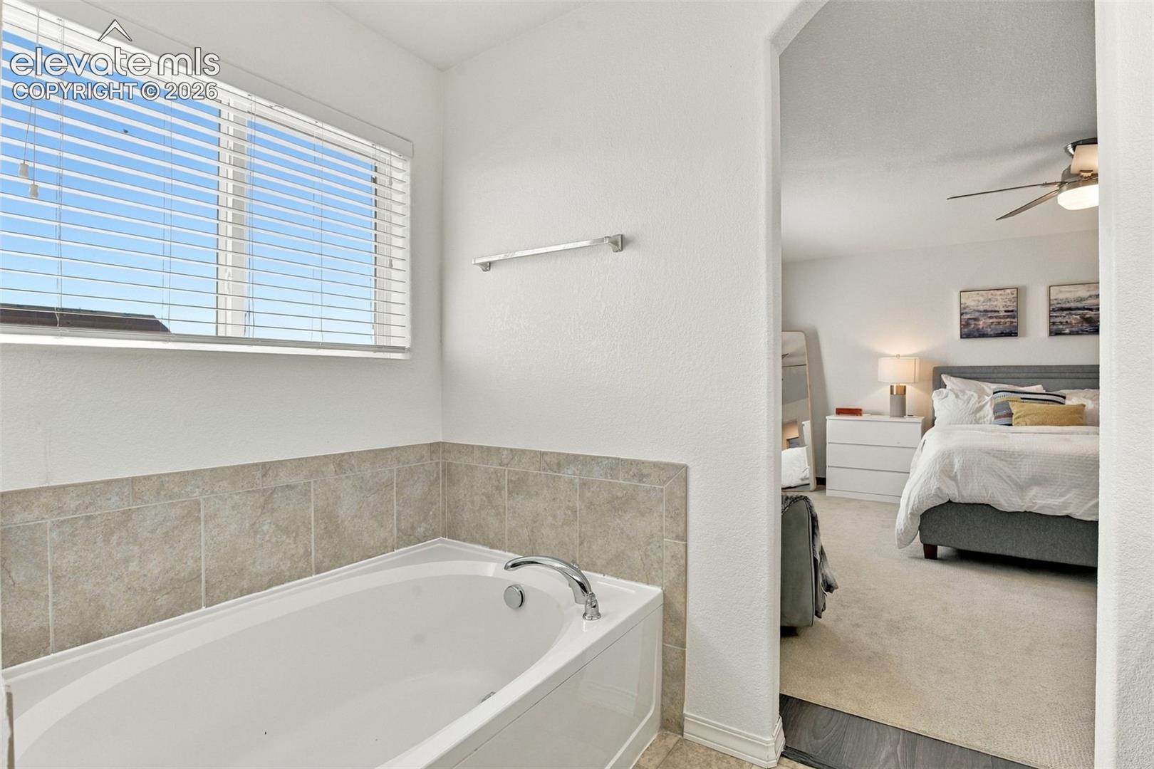 Built-in soaking tub with tile surround, window with horizontal blinds, and chrome fixtures