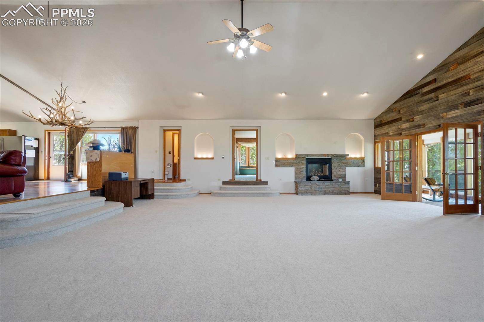 Spacious interior featuring a stone fireplace with arched niches, wood-finish accent wall, multiple French doors, and vaulted ceilings