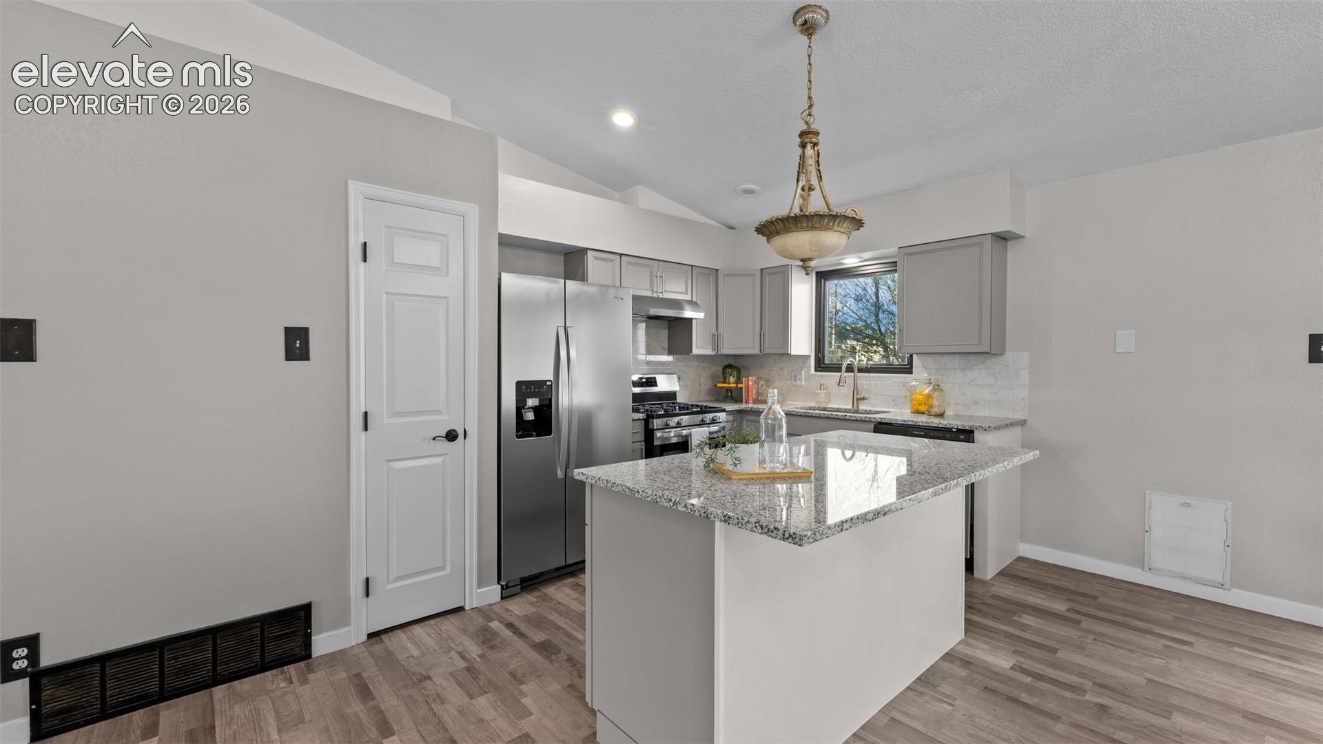 Kitchen featuring a central island with stone-finish countertop, stainless steel appliances, neutral-toned cabinetry, and decorative metal chandelier
