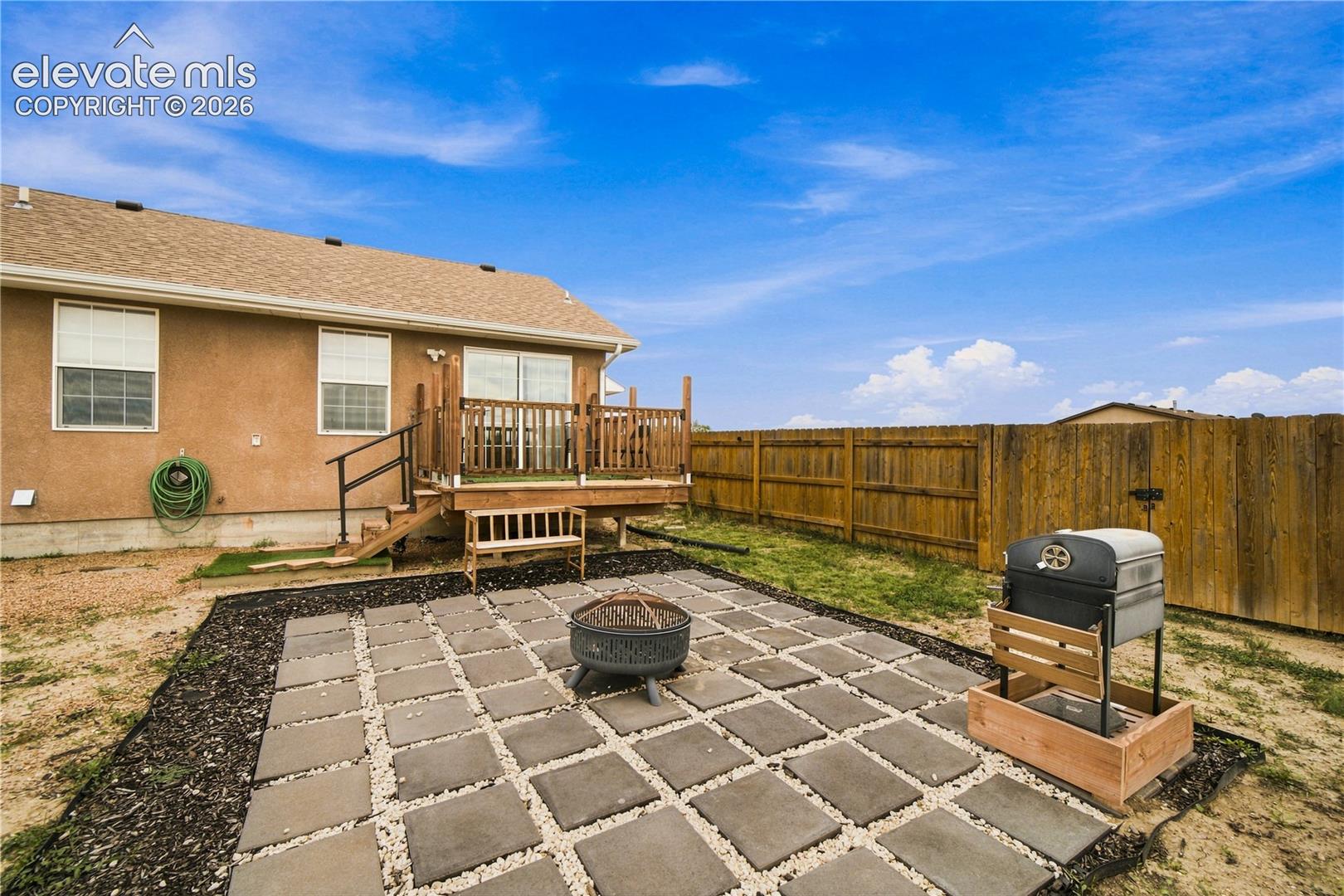 Expansive backyard featuring a wood privacy fence, a multi-level wood deck, and a paver patio with a fire pit