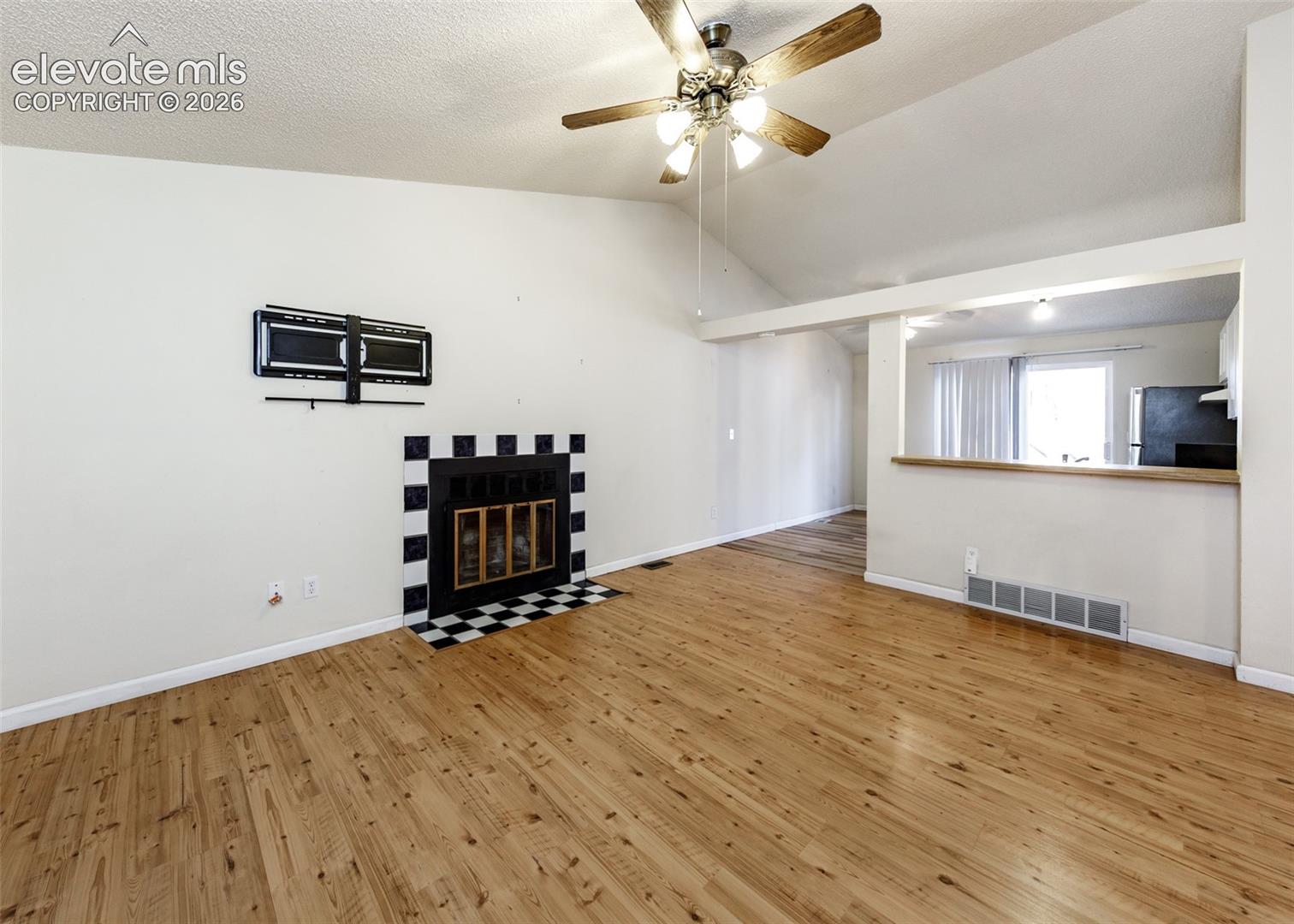 Vaulted ceiling featuring a central ceiling fan with integrated lighting, wood-finish flooring, and a fireplace with a decorative tile surround