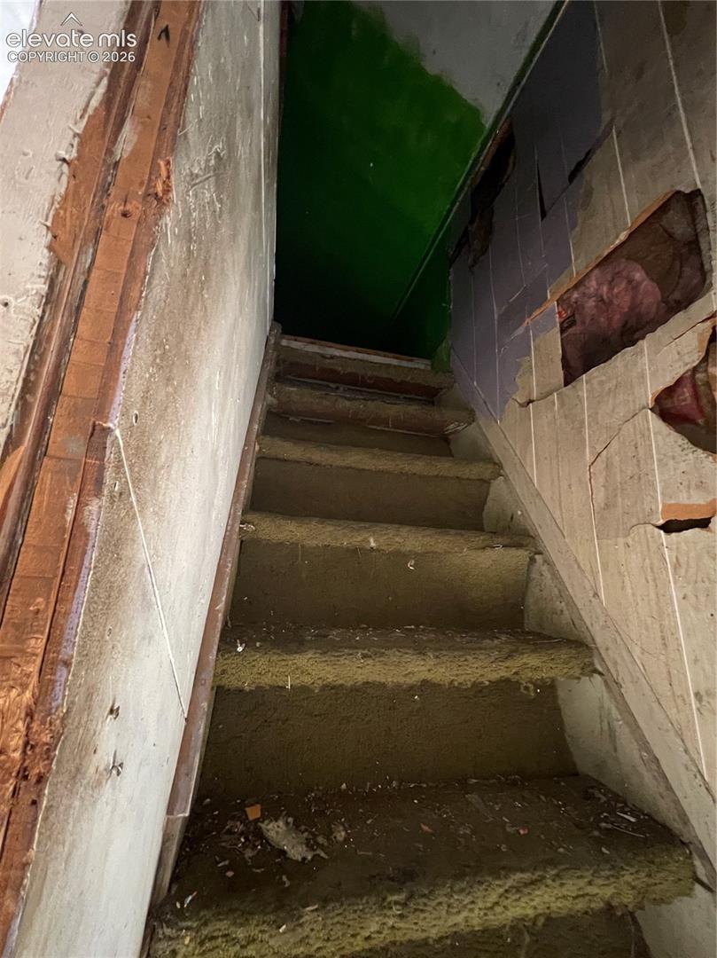 Staircase with exposed structural framing, drywall sections, and unfinished surfaces