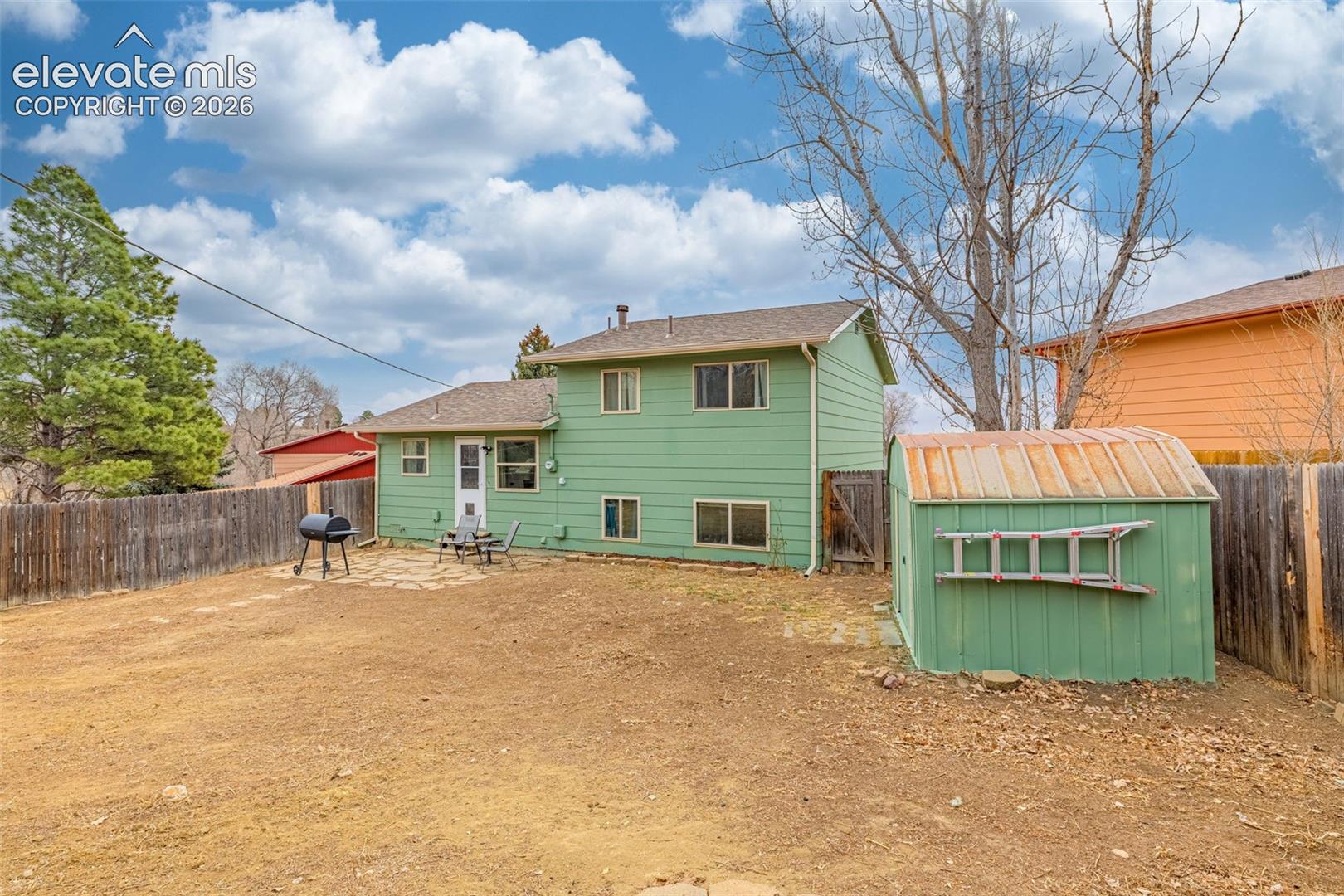 Rear exterior featuring green horizontal lap siding, a flagstone patio, a metal storage shed, and enclosed wood fencing