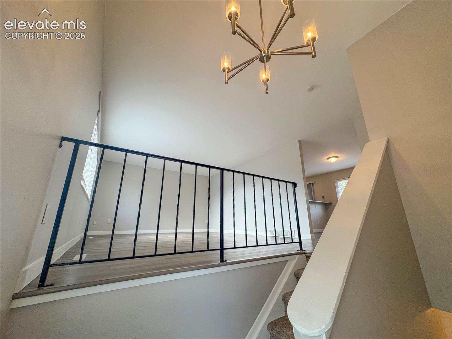 Vaulted ceilings, iron-spindle railing, wood-finish flooring, and a multi-arm pendant light fixture